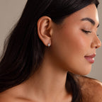 A woman with long dark hair, eyes closed in profile, wears the Celestial Sun Huggies in Silver—small star-shaped earrings that radiate subtle, statement charm.