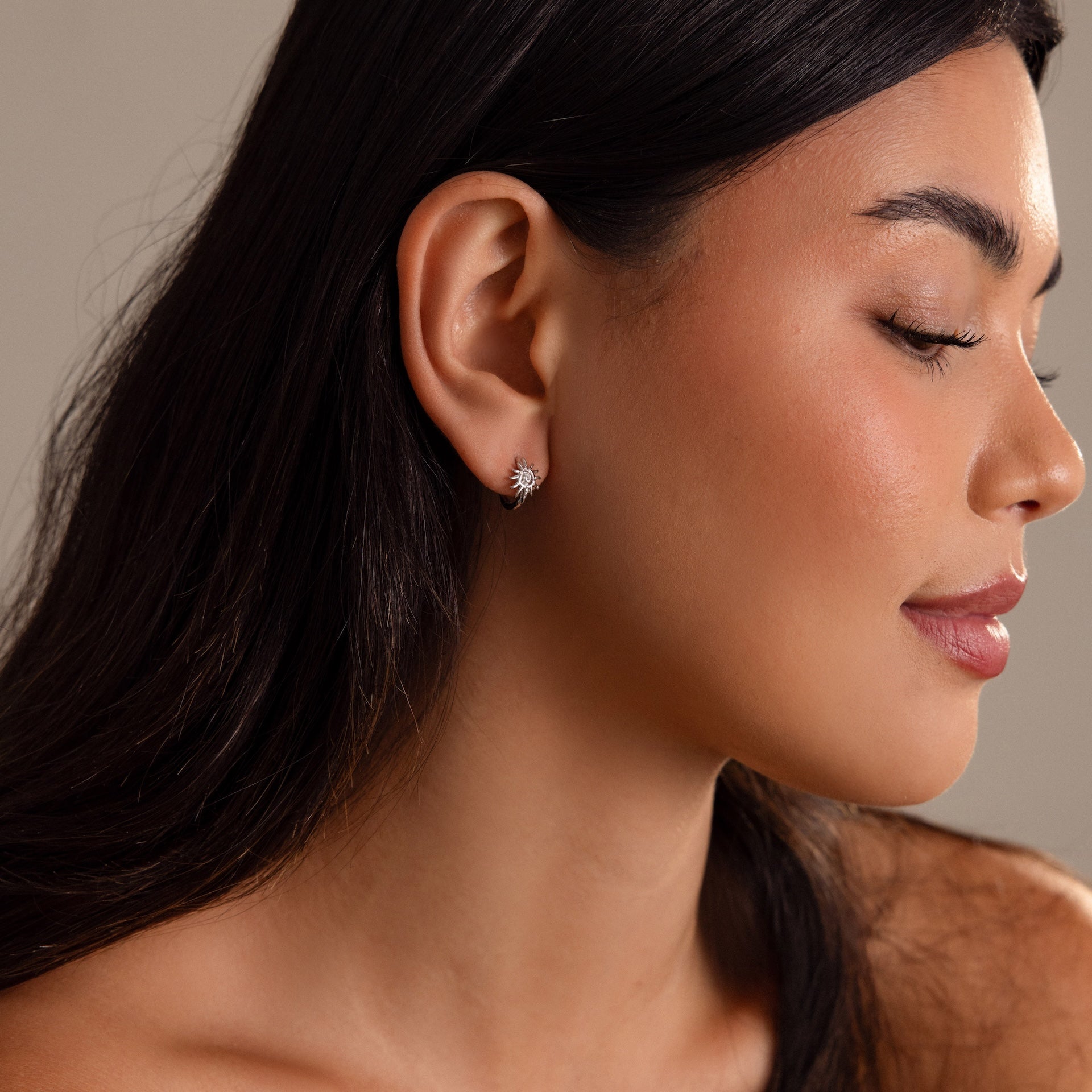 Woman with long dark hair, eyes closed, facing right, wears Celestial Sun Huggies—small, sparkling earrings for an elegant statement.