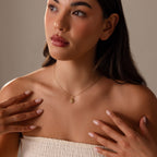 A woman wearing a strapless top and the Celestial Sun Necklace in 18K Gold touches her collarbone while looking to the side.