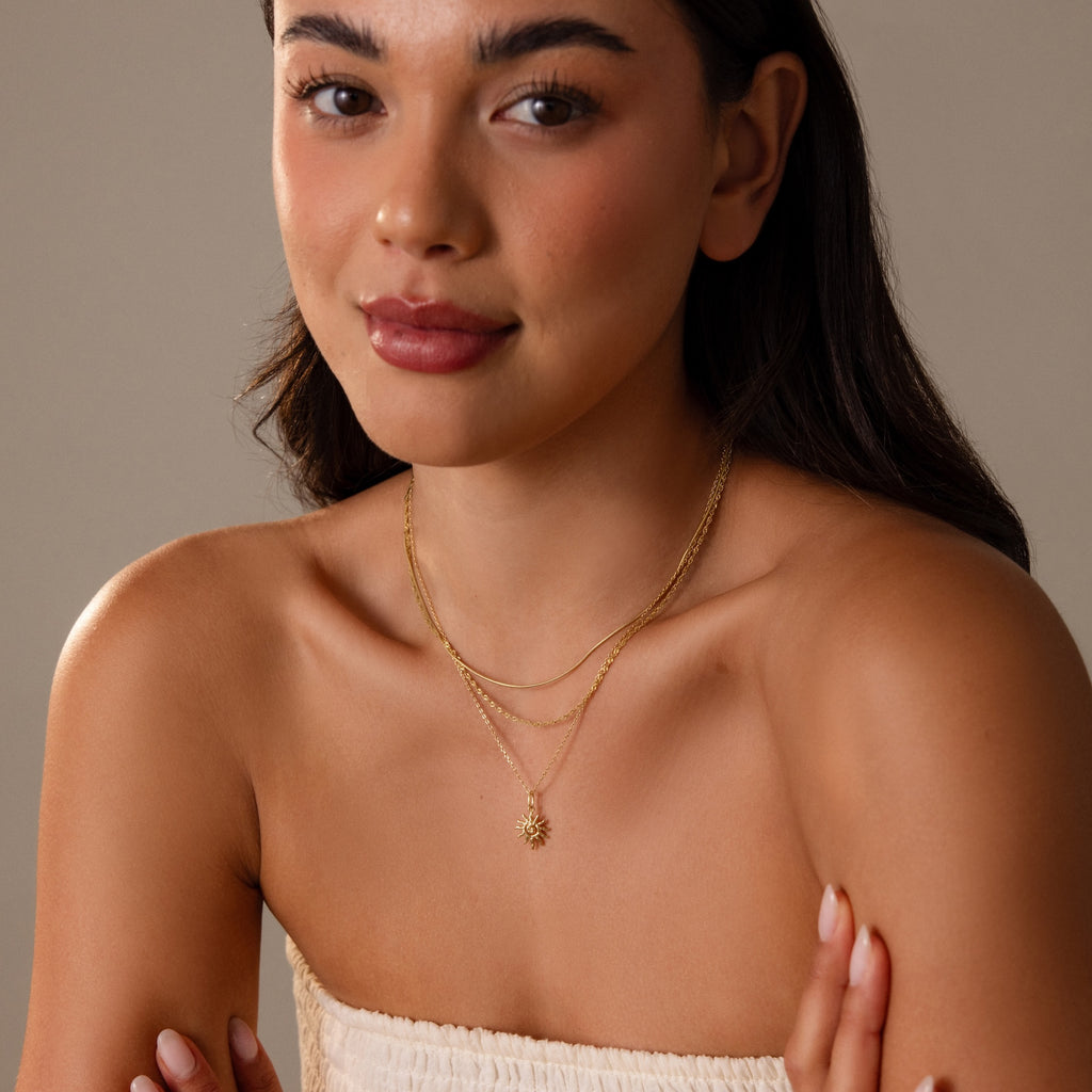 Woman with long dark hair, smiling softly, wears a layered Celestial Sun Necklace in 18K Gold and a strapless cream top.