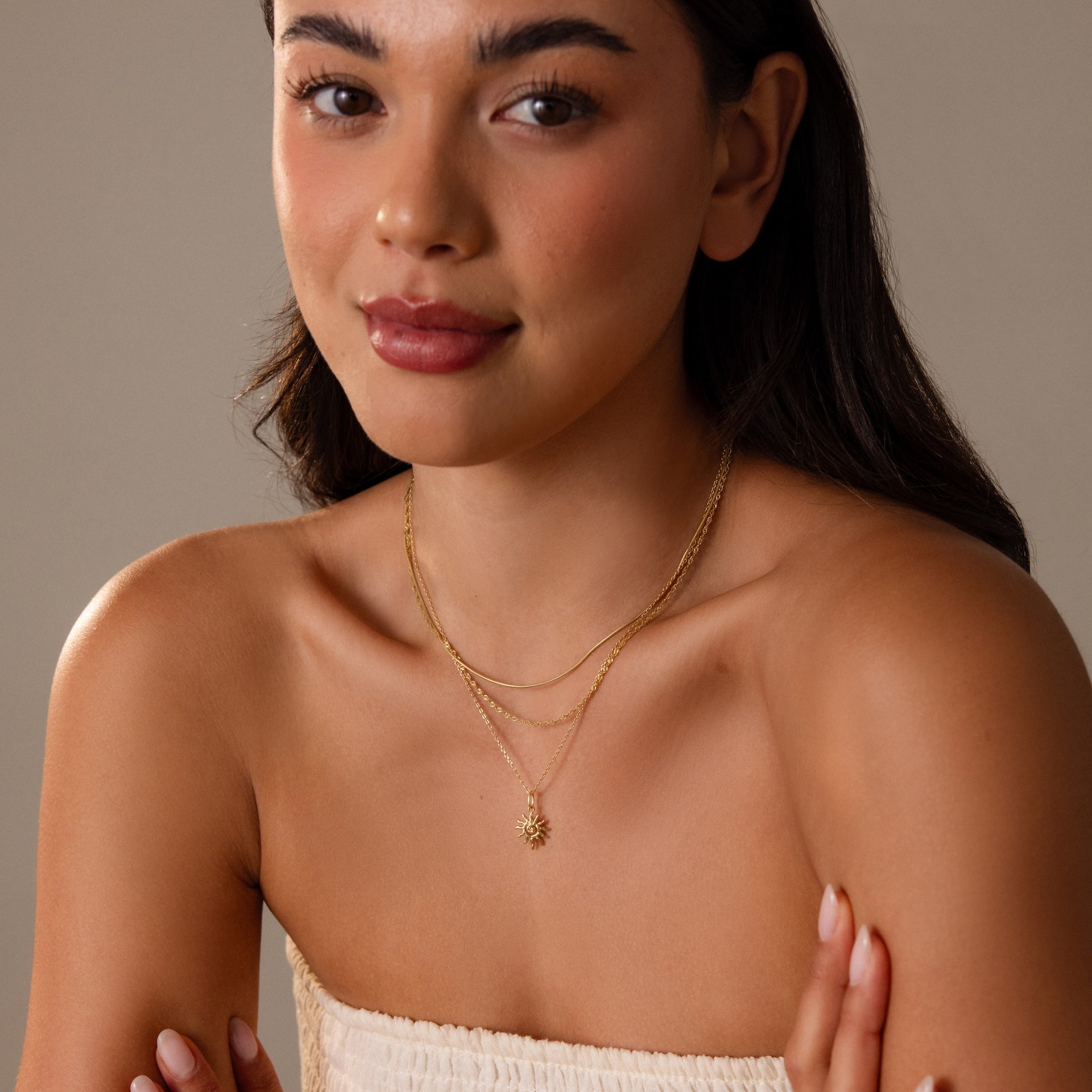 Woman with long dark hair, smiling softly, wears a layered Celestial Sun Necklace in 18K Gold and a strapless cream top.