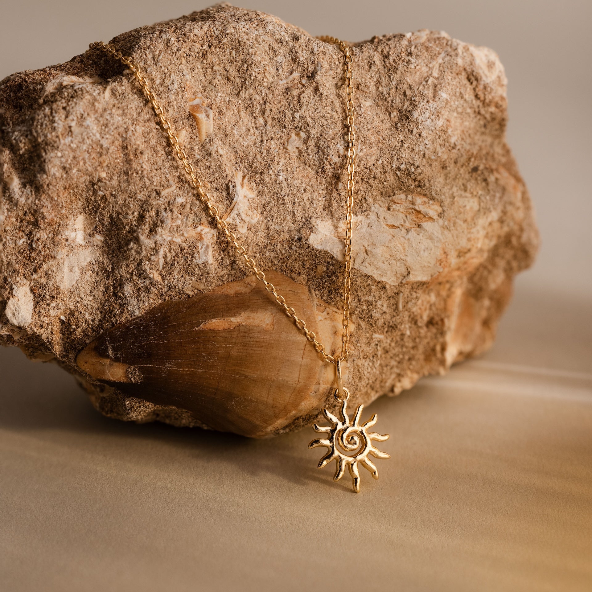 The Celestial Sun Necklace in 18K Gold, draped over a rough stone on a neutral background, features a sunburst pendant that creates an eye-catching statement look.