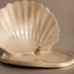 Diamond Seashell Charm Necklace in 18K Gold, displayed on a ceramic shell dish—an elegant piece of coastal jewelry, perfect for ocean lovers.