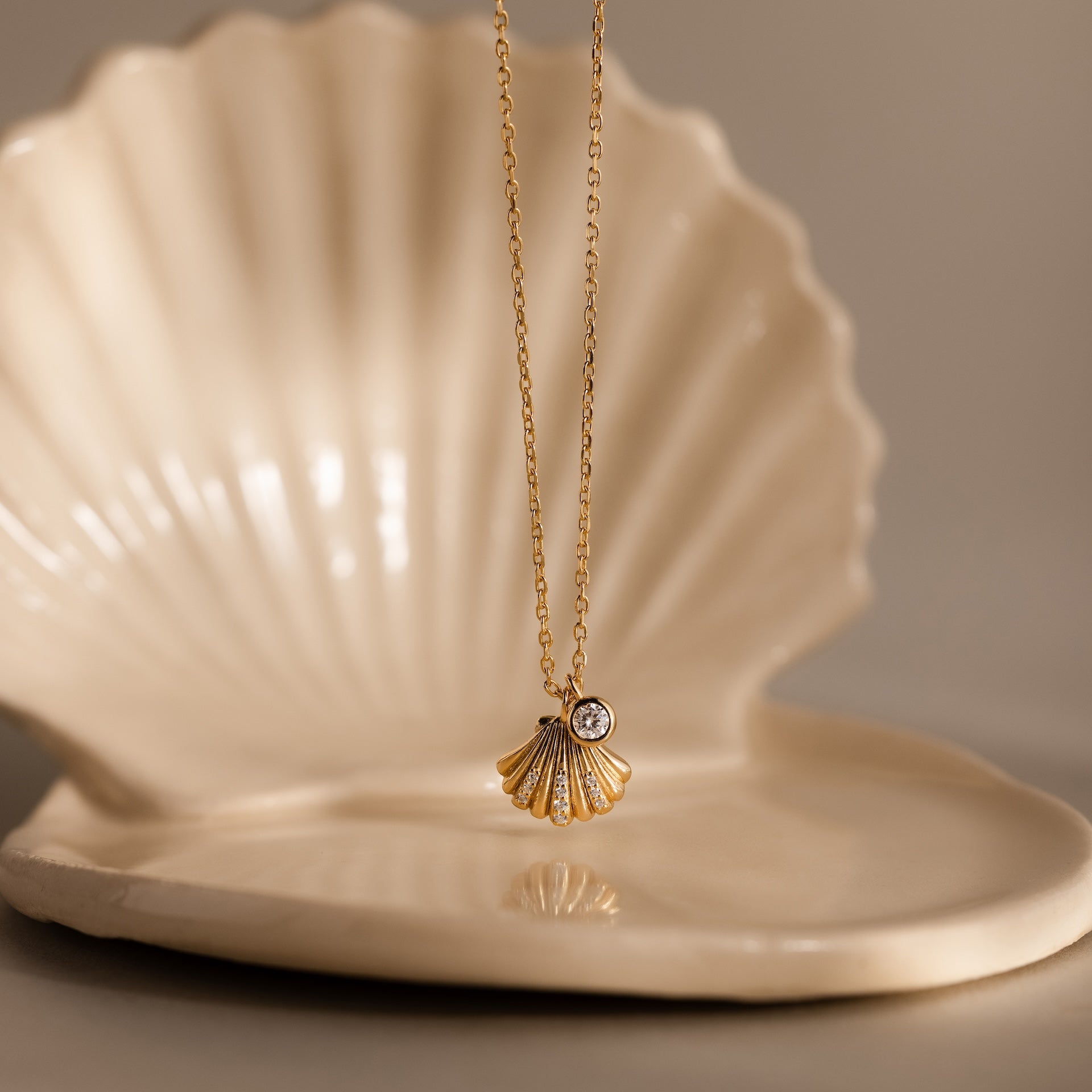 Diamond Seashell Charm Necklace in 18K Gold, displayed on a ceramic shell dish—an elegant piece of coastal jewelry, perfect for ocean lovers.