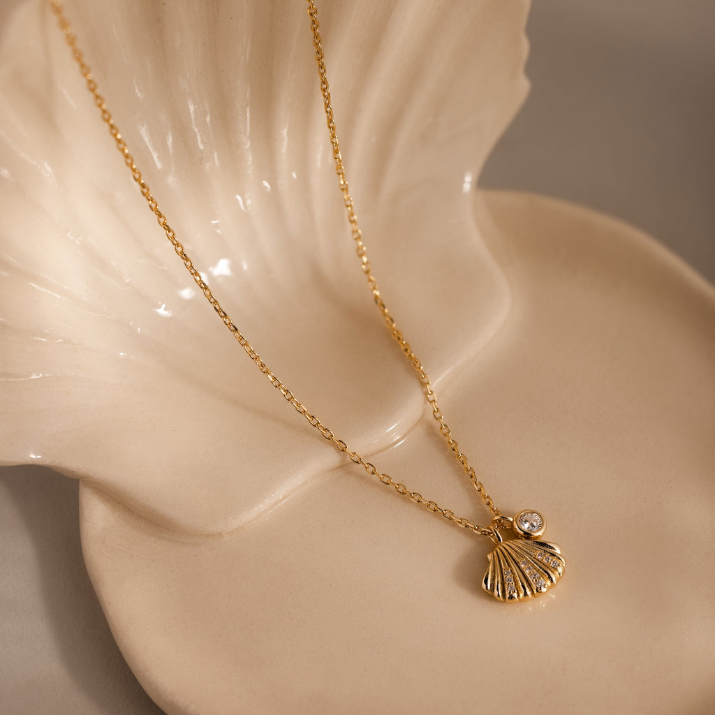 Diamond Seashell Charm Necklace in 18K Gold, shown on a cream ceramic shell dish—ideal coastal jewelry to complement any ocean-inspired look.
