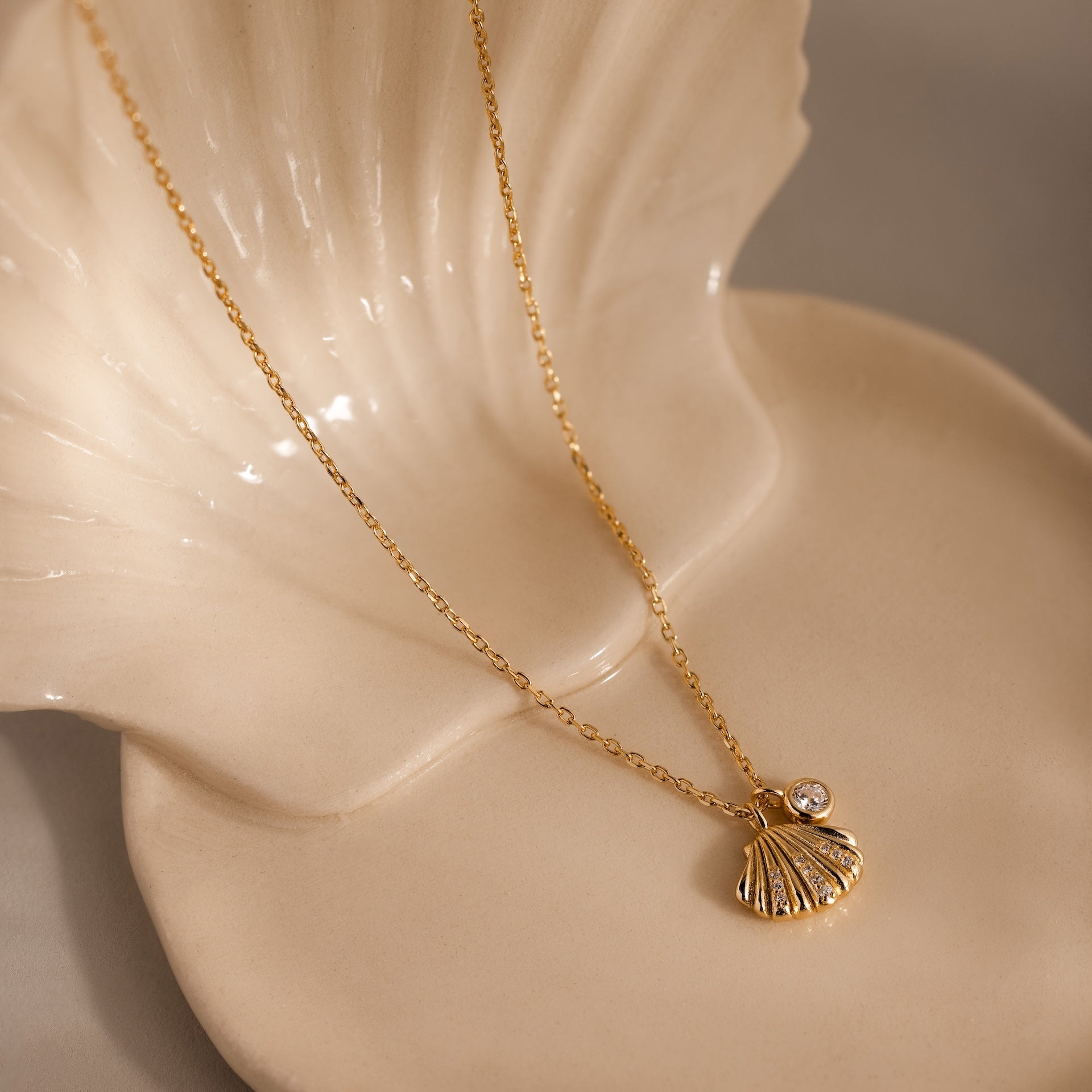 Diamond Seashell Charm Necklace in 18K Gold, shown on a cream ceramic shell dish—ideal coastal jewelry to complement any ocean-inspired look.