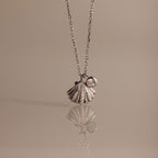 The Diamond Seashell Charm Necklace in Silver features a shell pendant and a small round gemstone, displayed on a neutral background—an elegant accessory to elevate any look.
