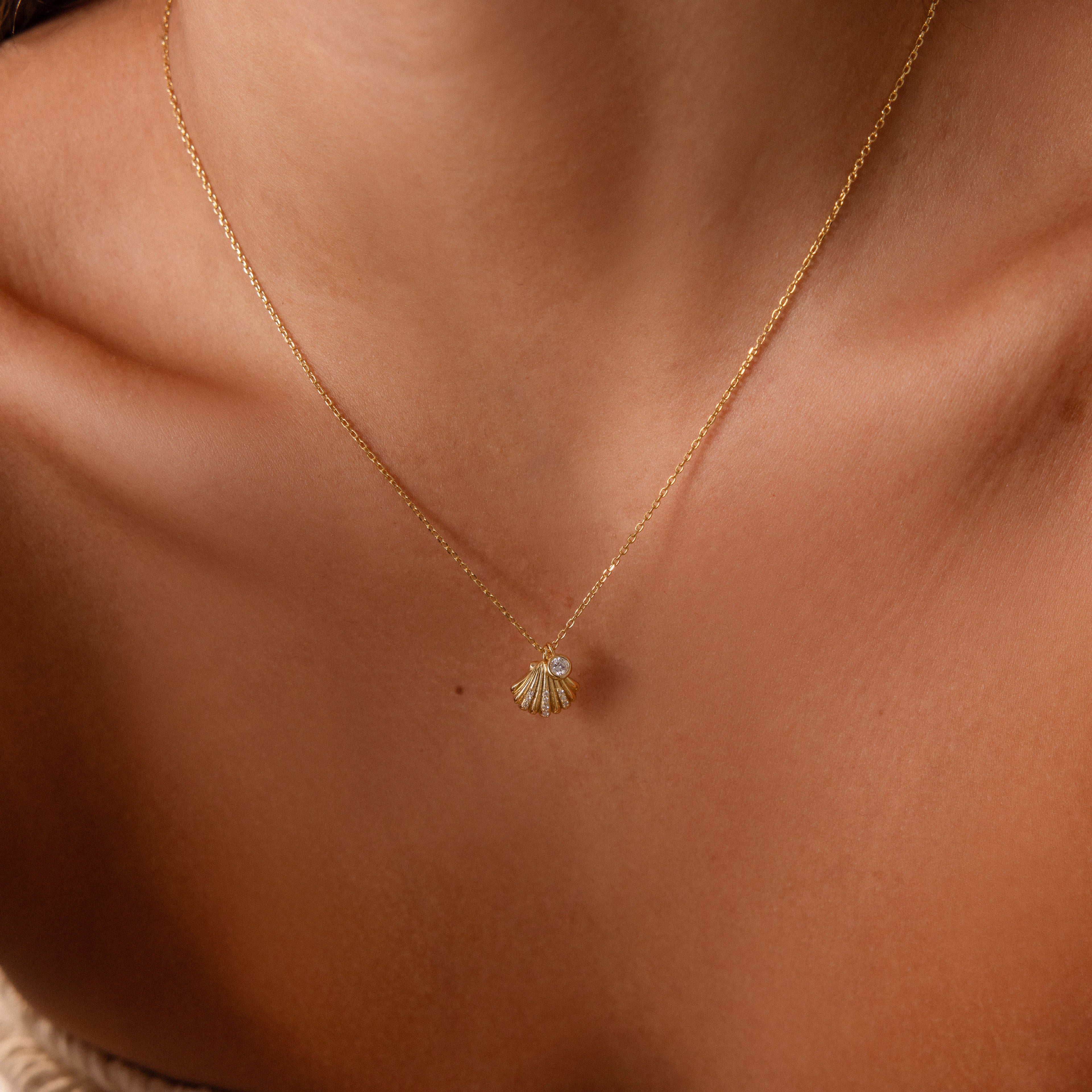 The Diamond Seashell Charm Necklace is a beautiful gold chain with a delicate seashell pendant, perfect for adding coastal charm to any womans style.