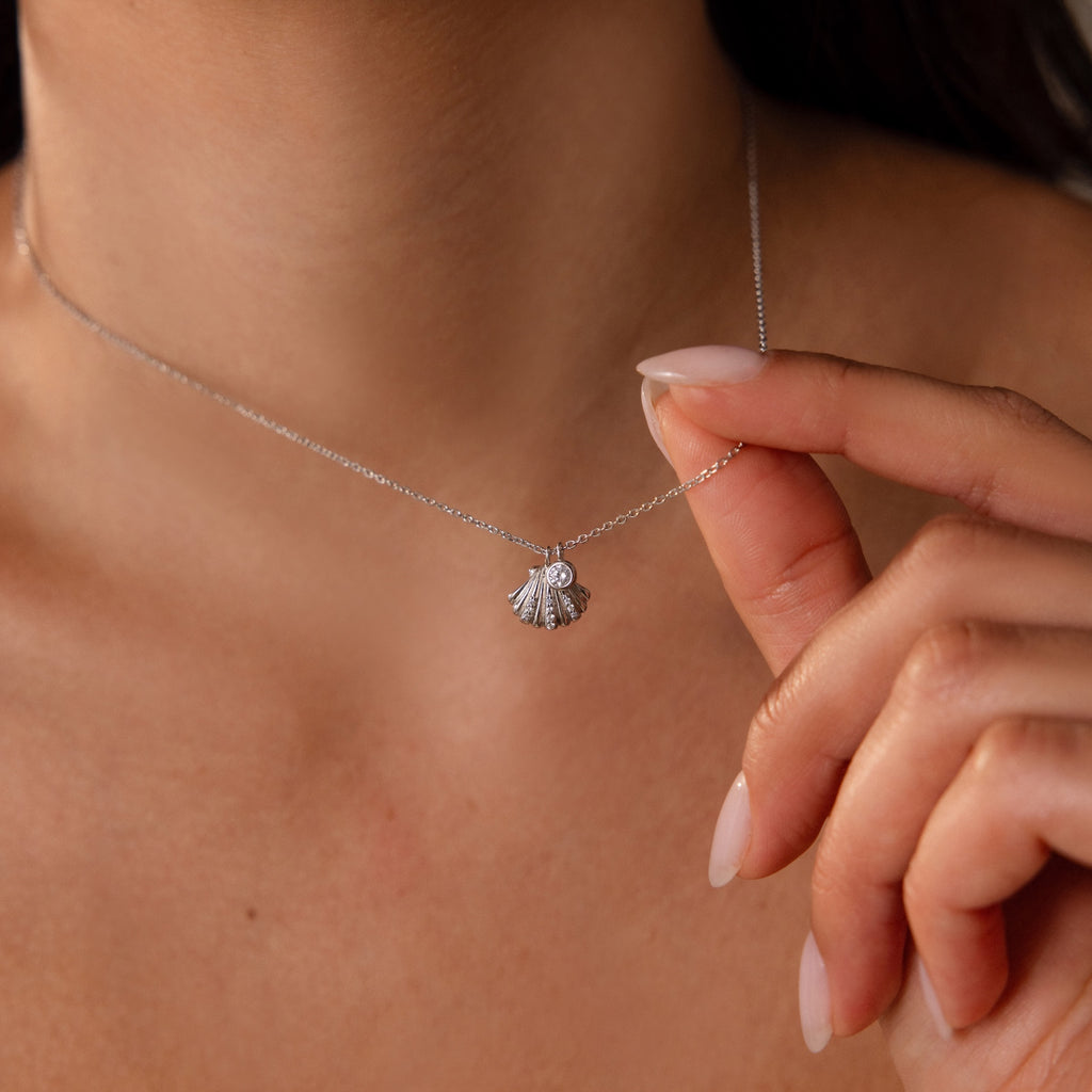 A woman wears the Diamond Seashell Charm Necklace, featuring a delicate seashell pendant resting against her neck.