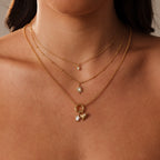 A woman wears three layered gold necklaces with small gemstone pendants and an Opal Sea Turtle Charm for an elegant, seaside-inspired look.