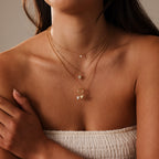 A woman wears the Opal Sea Turtle Charm layered with gold necklaces and a white textured strapless top for an ocean-inspired look.