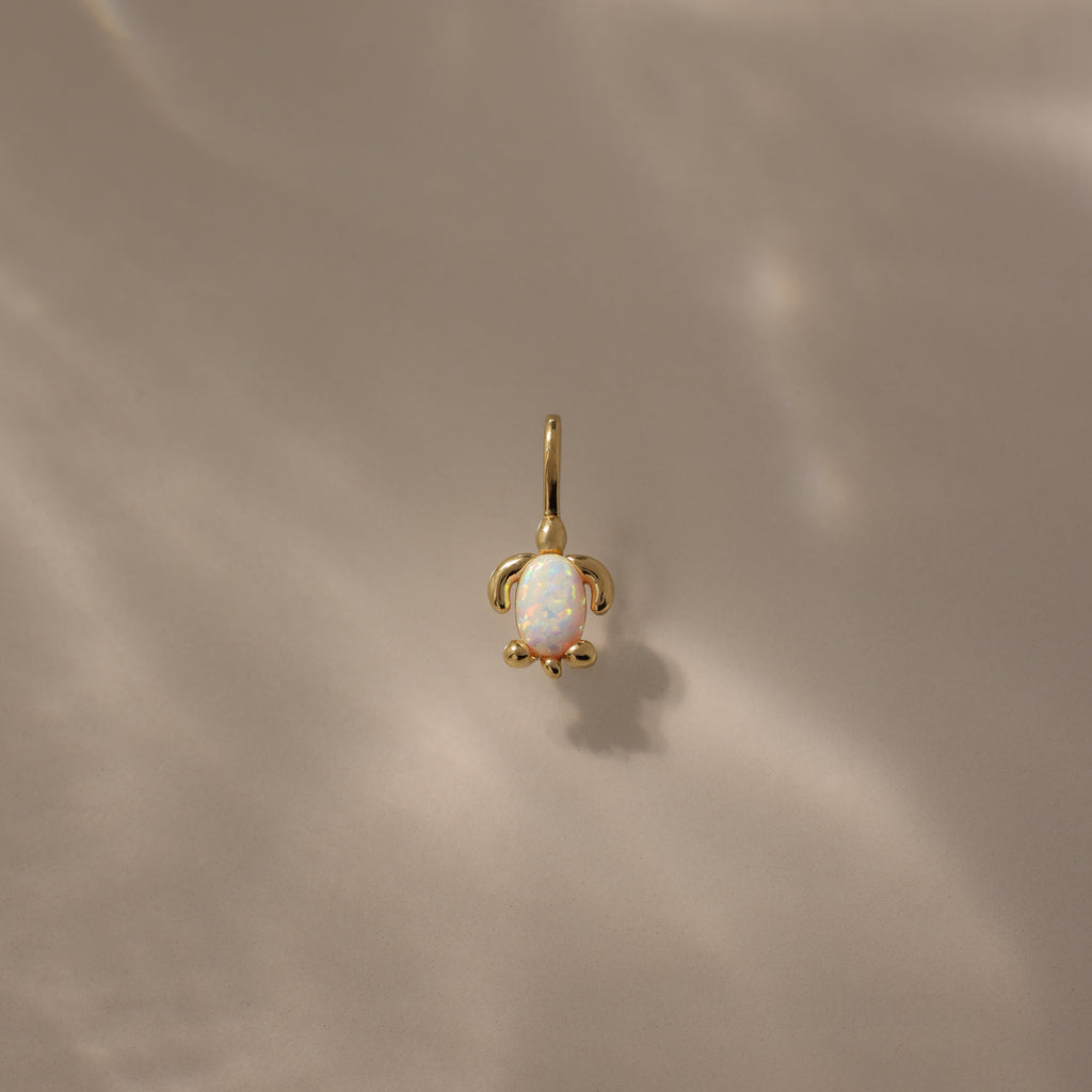 Opal Sea Turtle Charm in 18K Gold featuring an opal stone center, set against a soft beige background with ocean-inspired light reflections.
