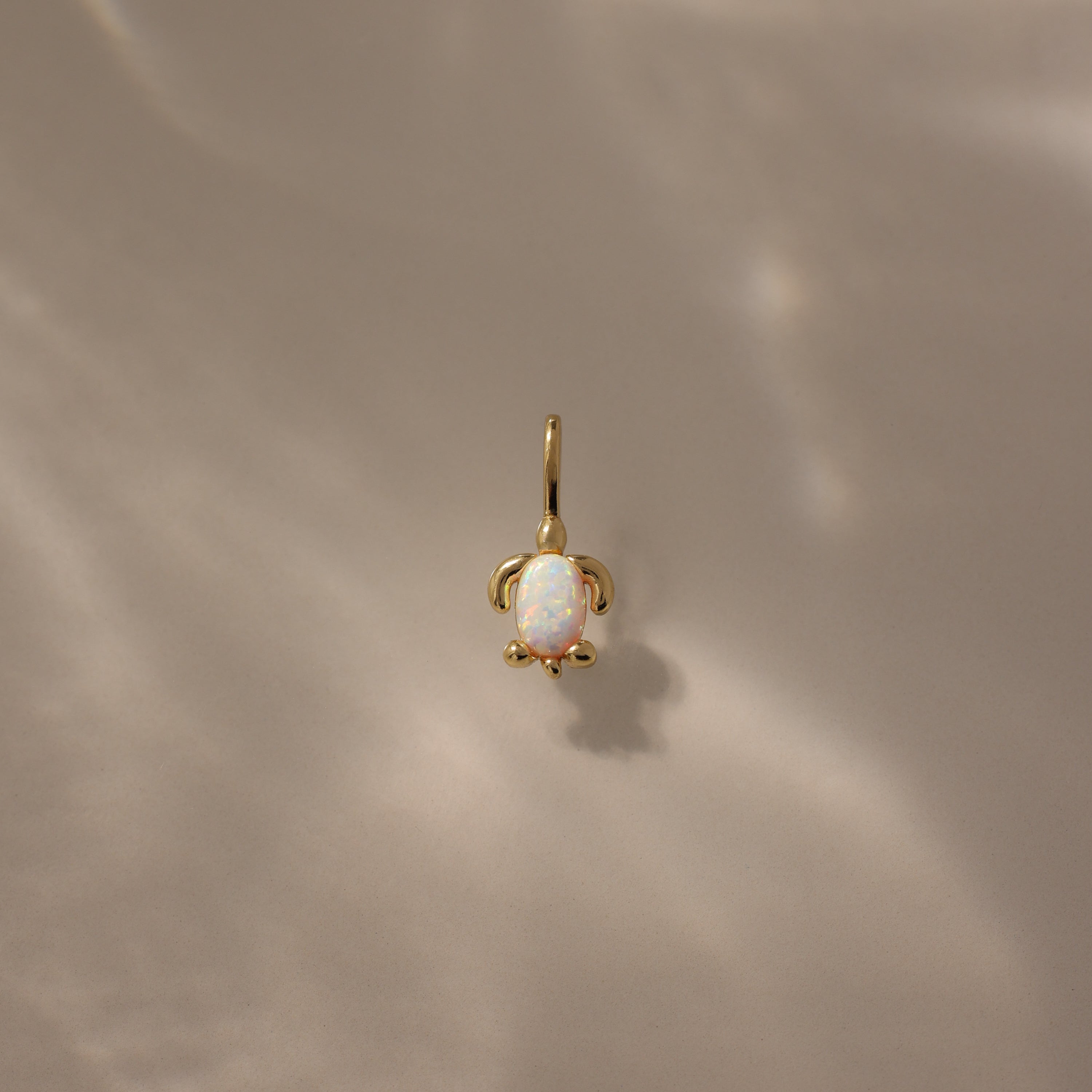 Opal Sea Turtle Charm in 18K Gold featuring an opal stone center, set against a soft beige background with ocean-inspired light reflections.