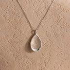 Organic Fingerprint Teardrop Necklace with a small green birthstone, displayed on a textured beige background—a personalized and uniquely charming jewelry piece.