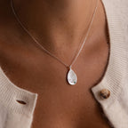 An Organic Fingerprint Teardrop Necklace is styled over a cream cardigan with a missing button.