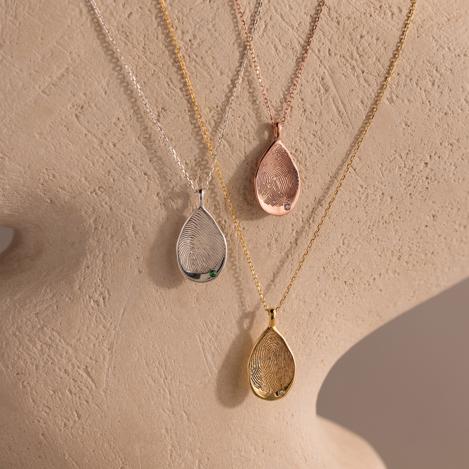 An Organic Fingerprint Teardrop Necklace in rose gold hangs on a textured display bust, capturing a unique personal touch in elegant form.