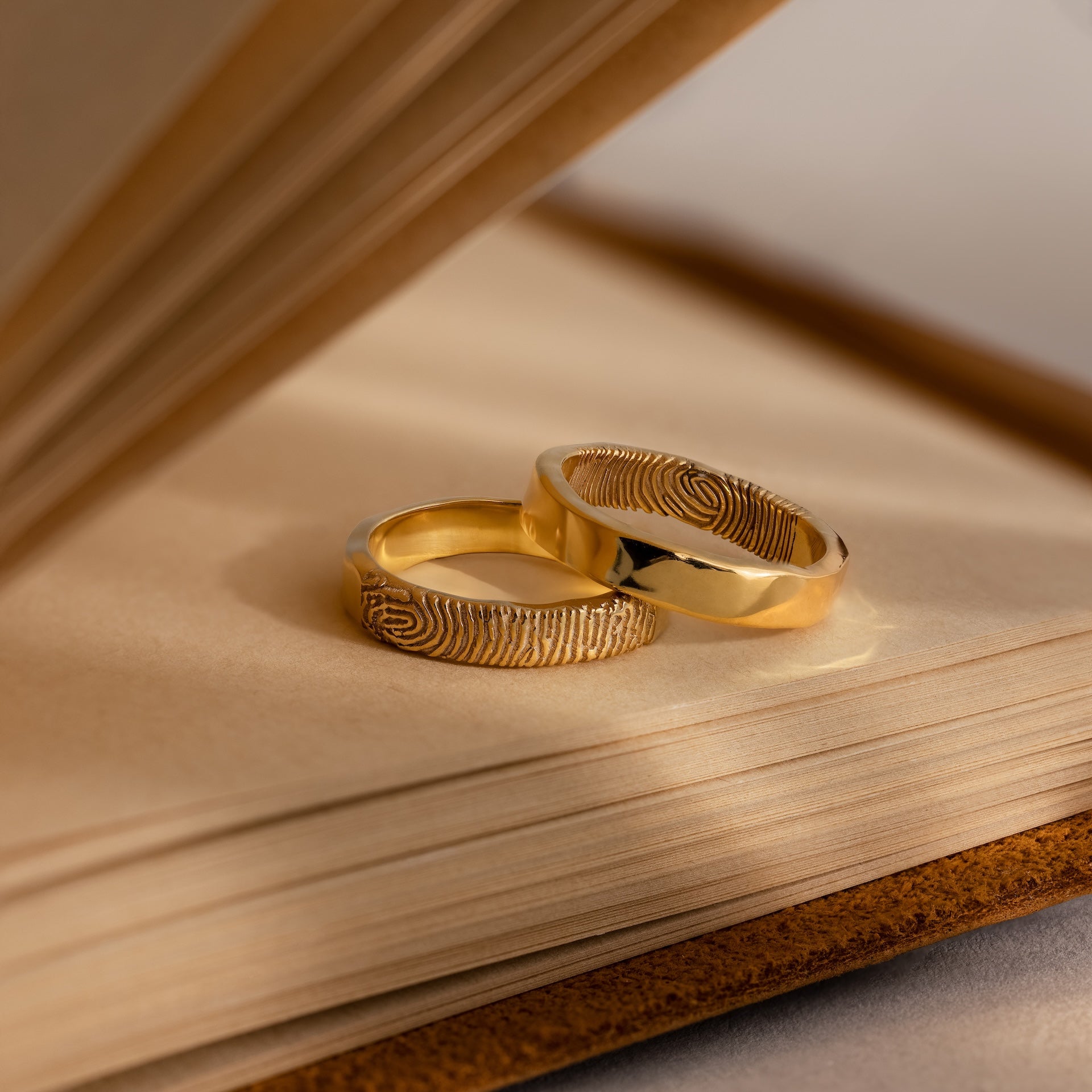 Two Organic Fingerprint Bands with custom-engraved patterns rest on the pages of an open book.