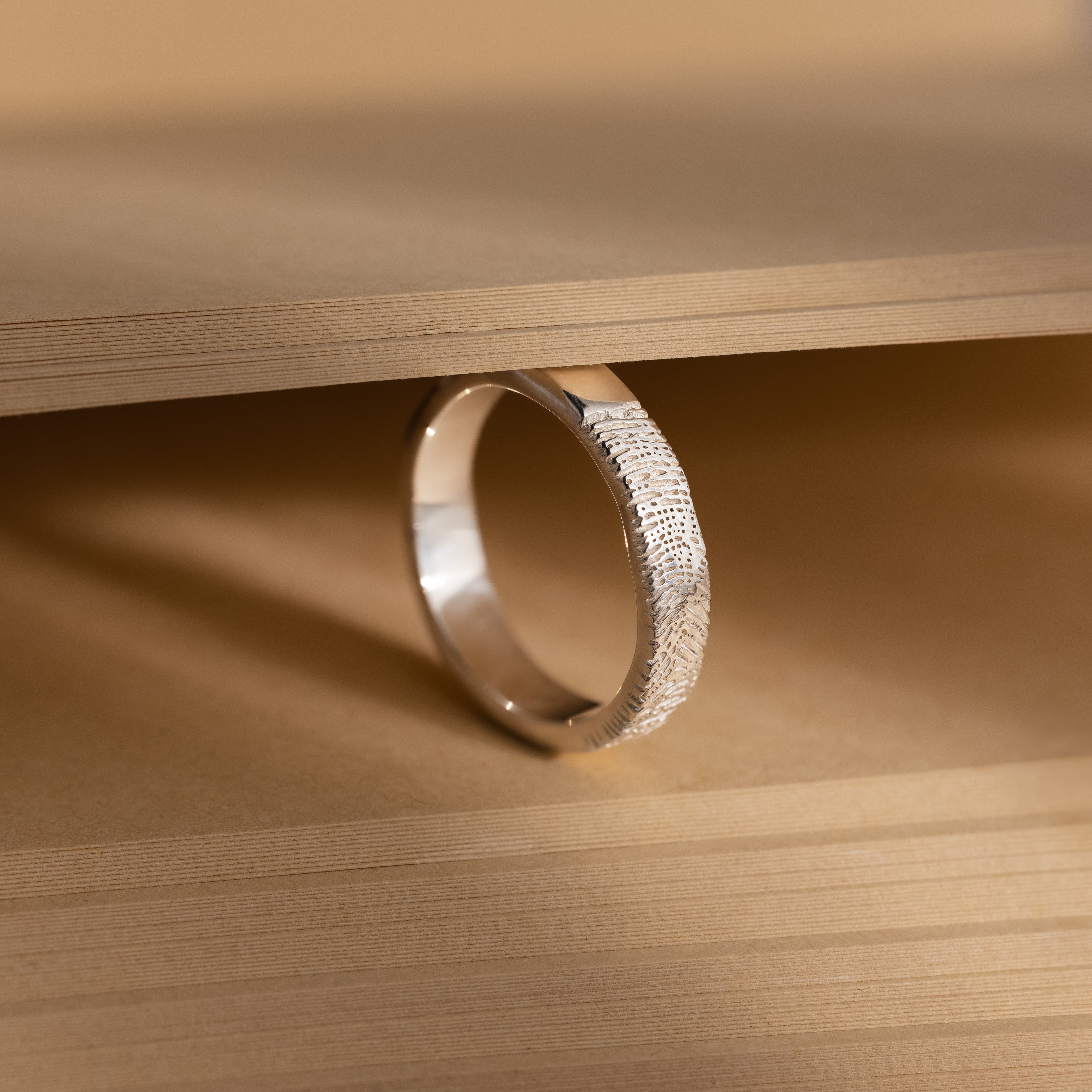 The Organic Fingerprint Band in Sterling Silver stands upright between stacked beige paper sheets, creating a unique memorial keepsake.