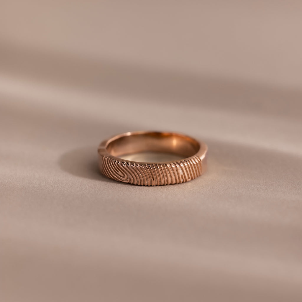 The Organic Fingerprint Band in Rose Gold, custom-engraved and displayed on a soft beige background, makes an elegant memorial keepsake to cherish forever.