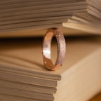 The Organic Fingerprint Band in Rose Gold stands upright between book pages, serving as a unique and memorable keepsake.