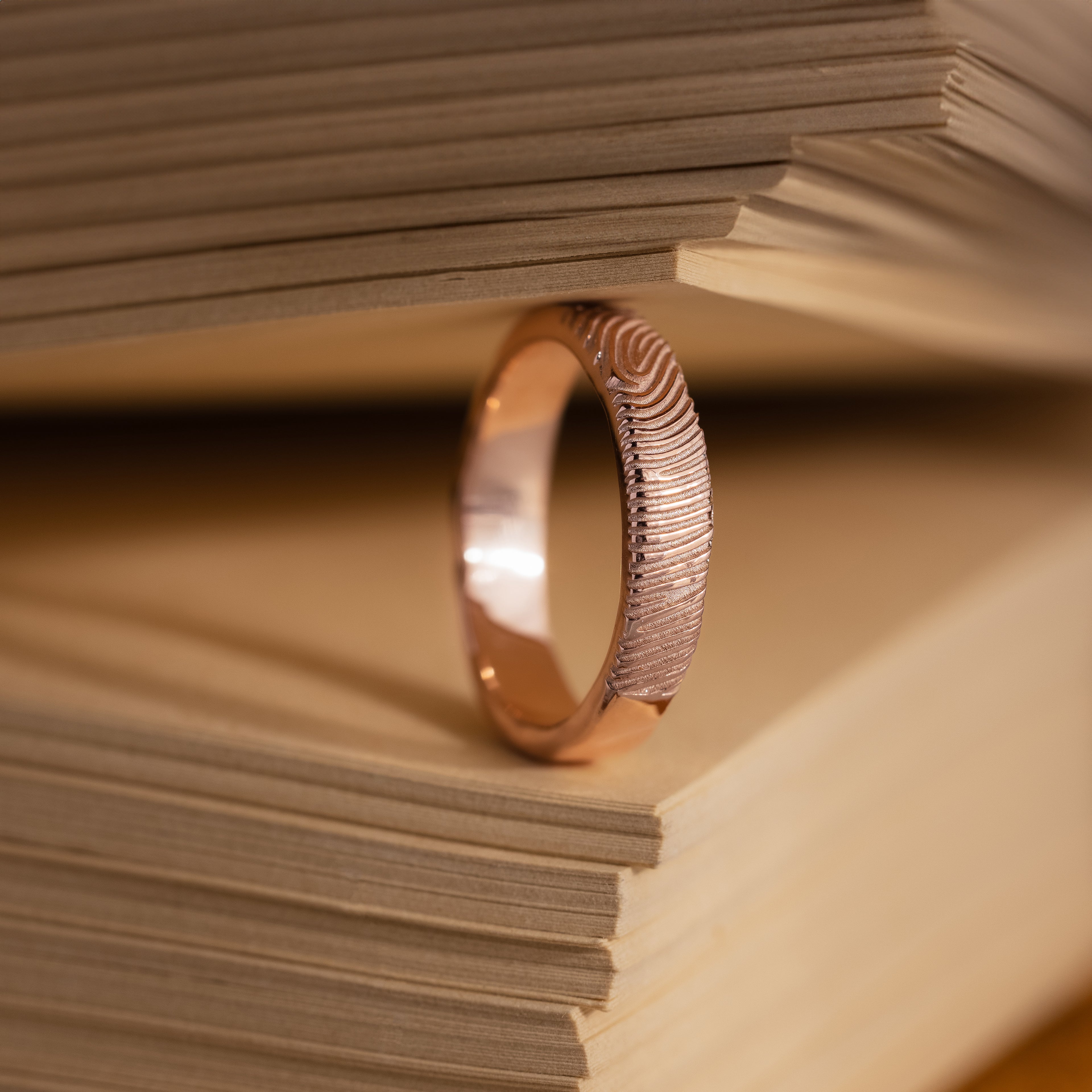 The Organic Fingerprint Band in Rose Gold stands upright between book pages, serving as a unique and memorable keepsake.