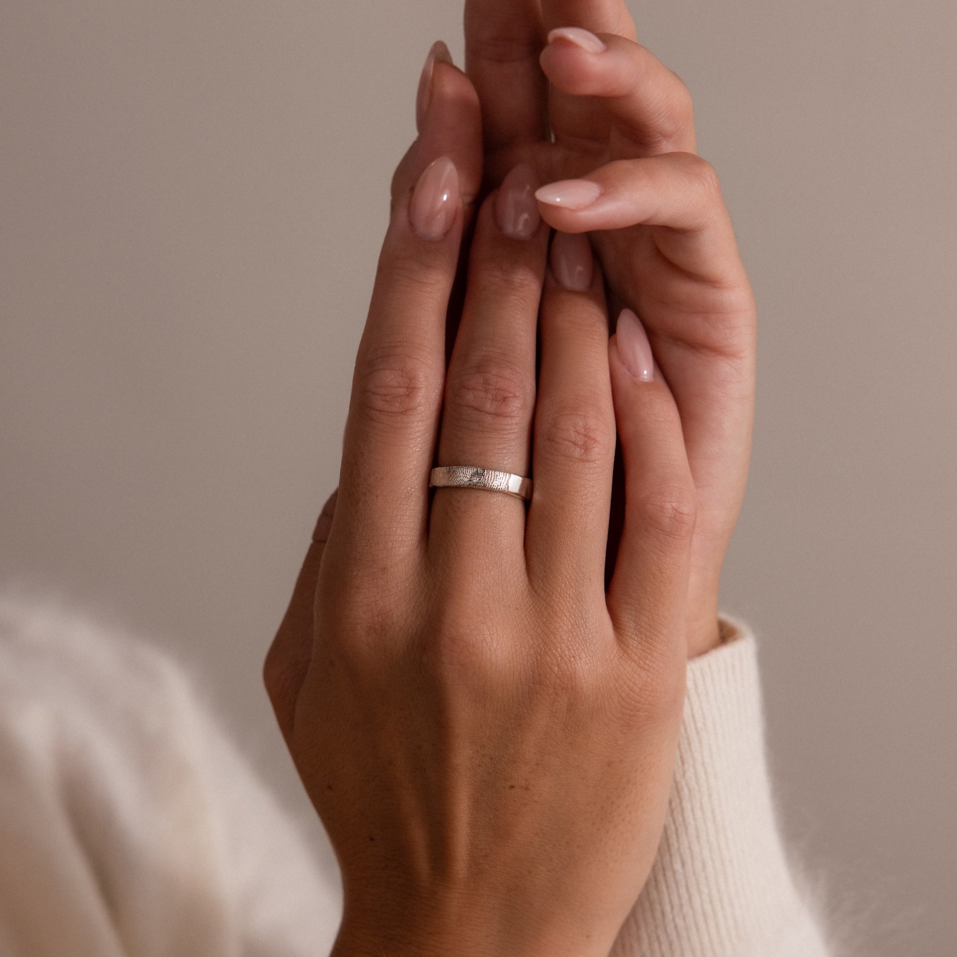 A close-up of manicured hands, one wearing the Organic Fingerprint Band in Sterling Silver, showcased against a neutral background.