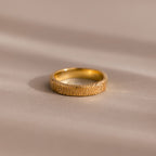 A custom-engraved Organic Fingerprint Band in 18K Gold rests on a smooth, beige surface—perfect as a memorial keepsake.