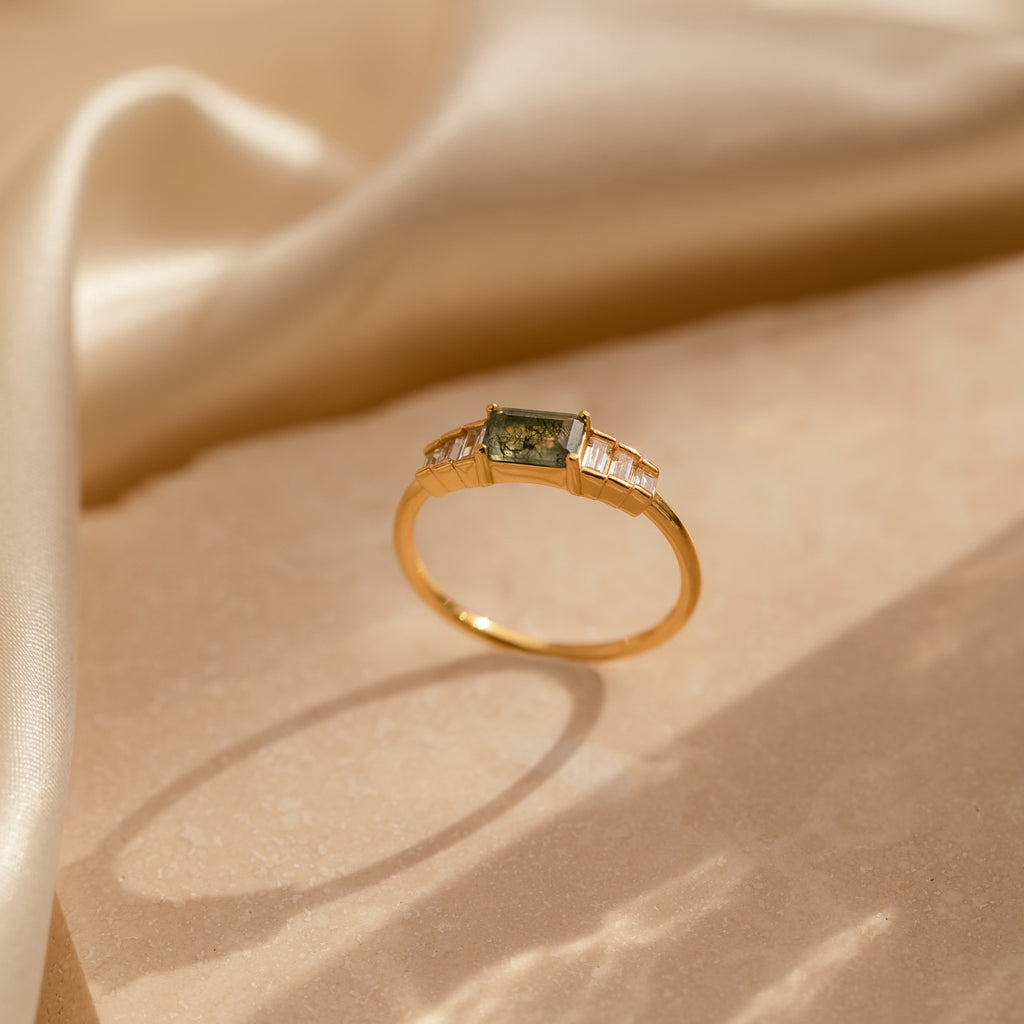 Upright view of the gold moss agate ring with light casting shadows around its circular base, emphasizing the natural patterns within the central stone.