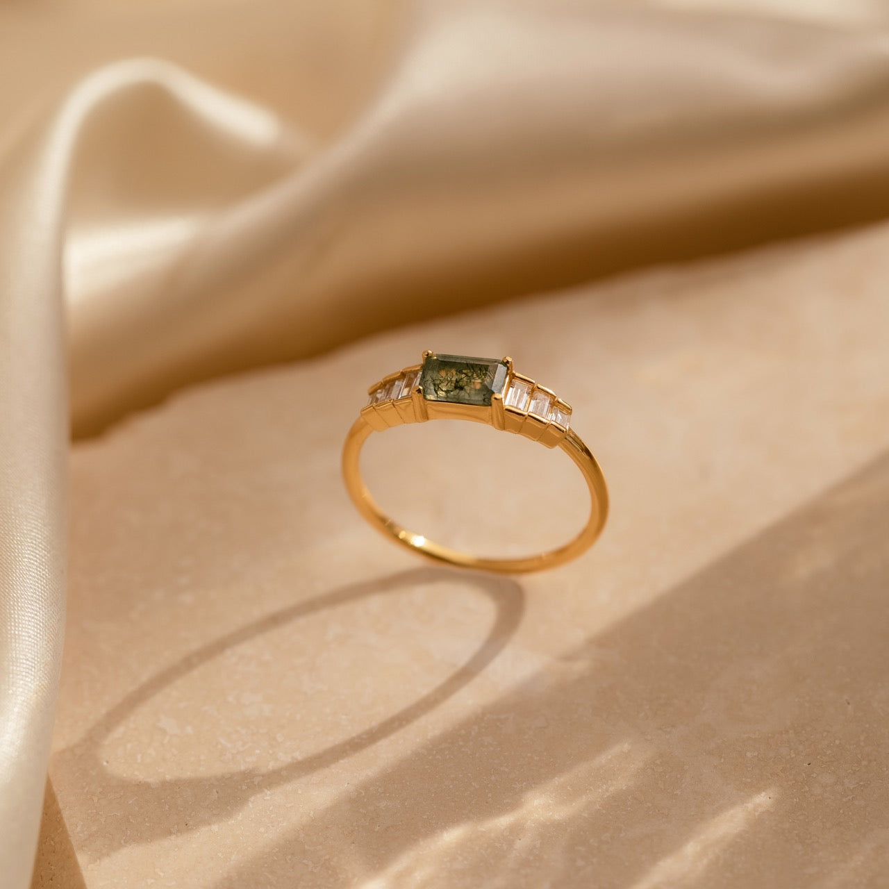 Upright view of the gold moss agate ring with light casting shadows around its circular base, emphasizing the natural patterns within the central stone.