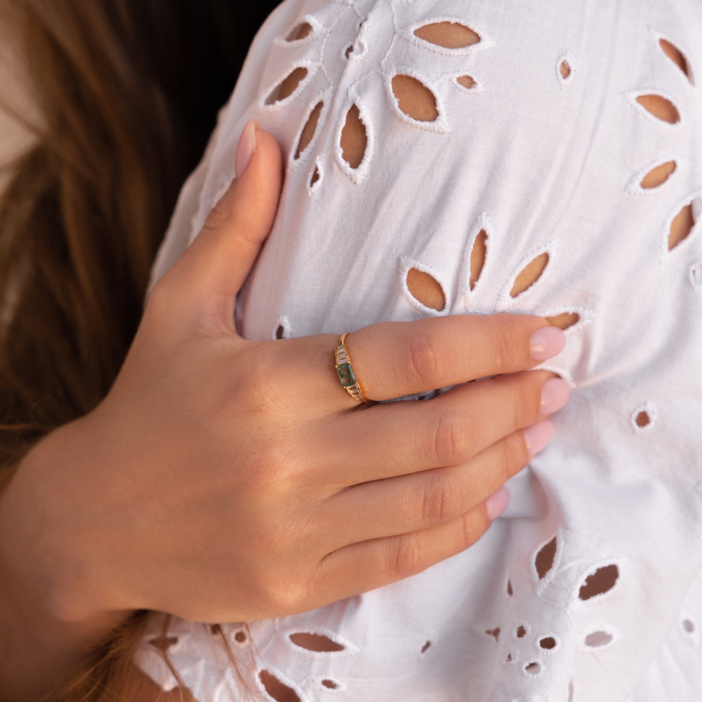Moss agate ring worn on the hand, gently placed over a white broderie anglaise dress, showing the subtle sparkle of the baguette accents.