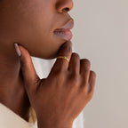 A person gently touches their chin, showcasing the Baguette Peridot Curb Ring with a bezel-set peridot gemstone on their finger.