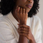 A woman in a white sweater rests her chin on her hand, showcasing the Baguette Topaz Curb Ring with pink bezel-set gemstones.