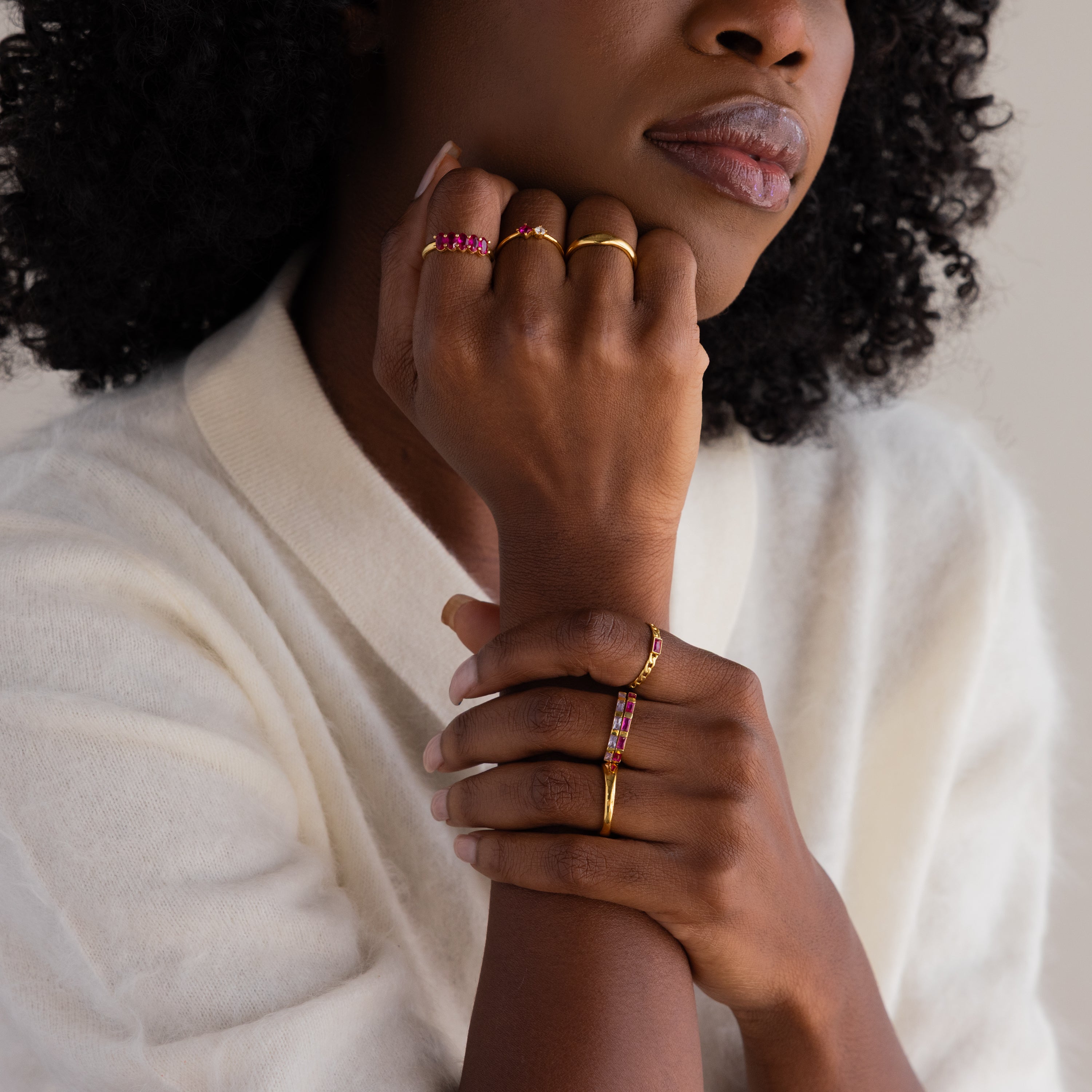A woman in a white sweater rests her chin on her hand, showcasing the Baguette Topaz Curb Ring with pink bezel-set gemstones.