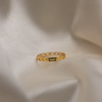 The Baguette Peridot Curb Ring, highlighted by its bezel-set gemstone, is displayed on soft, creamy draped fabric.