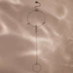 Delicate silver hand chain bracelet with small bezel-set stones displayed on a soft beige background with gentle shadows.