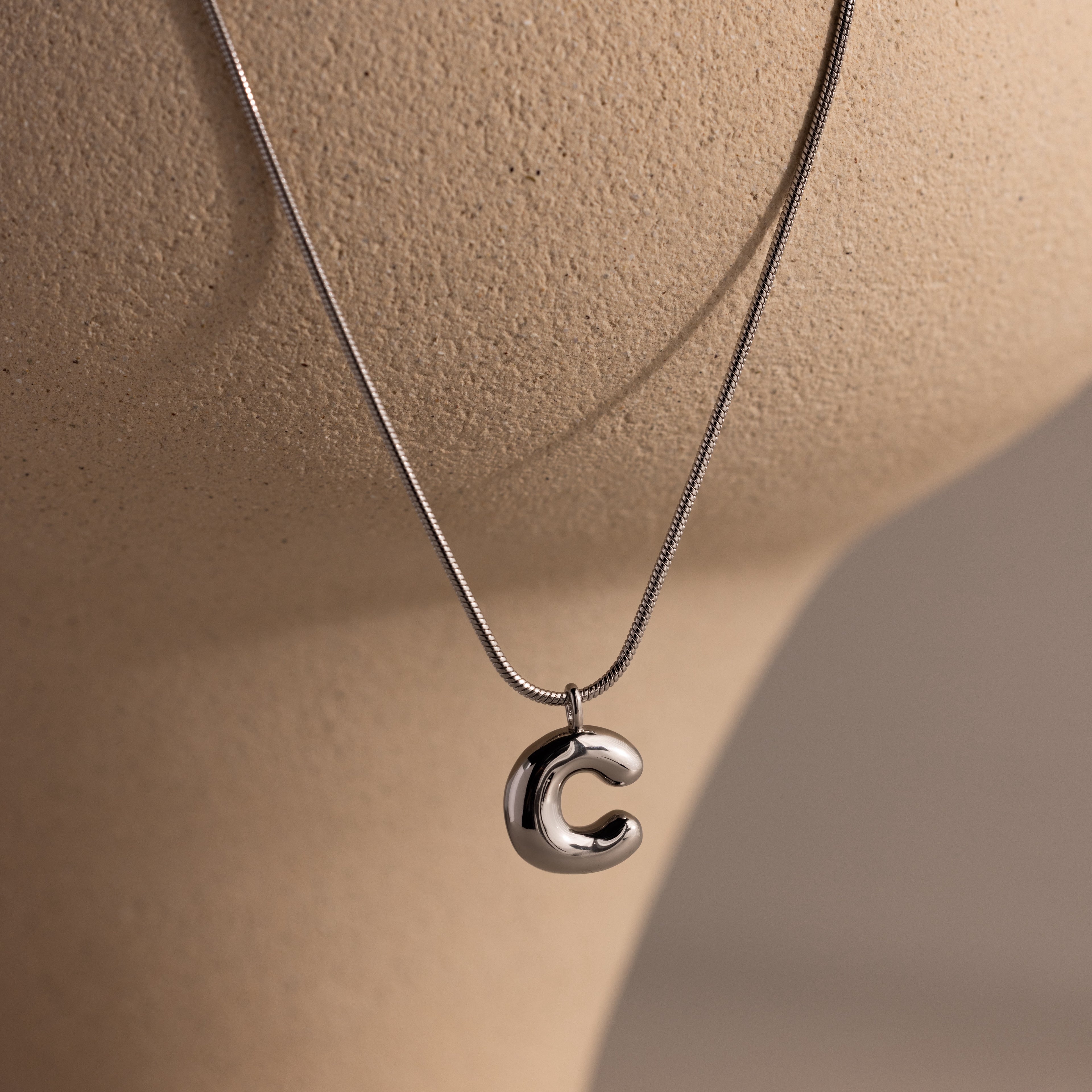 Bubble Letter Necklace in White Gold featuring a shiny letter C pendant, shown on a beige mannequin bust—ideal for adding a personalized jewelry touch to any outfit.