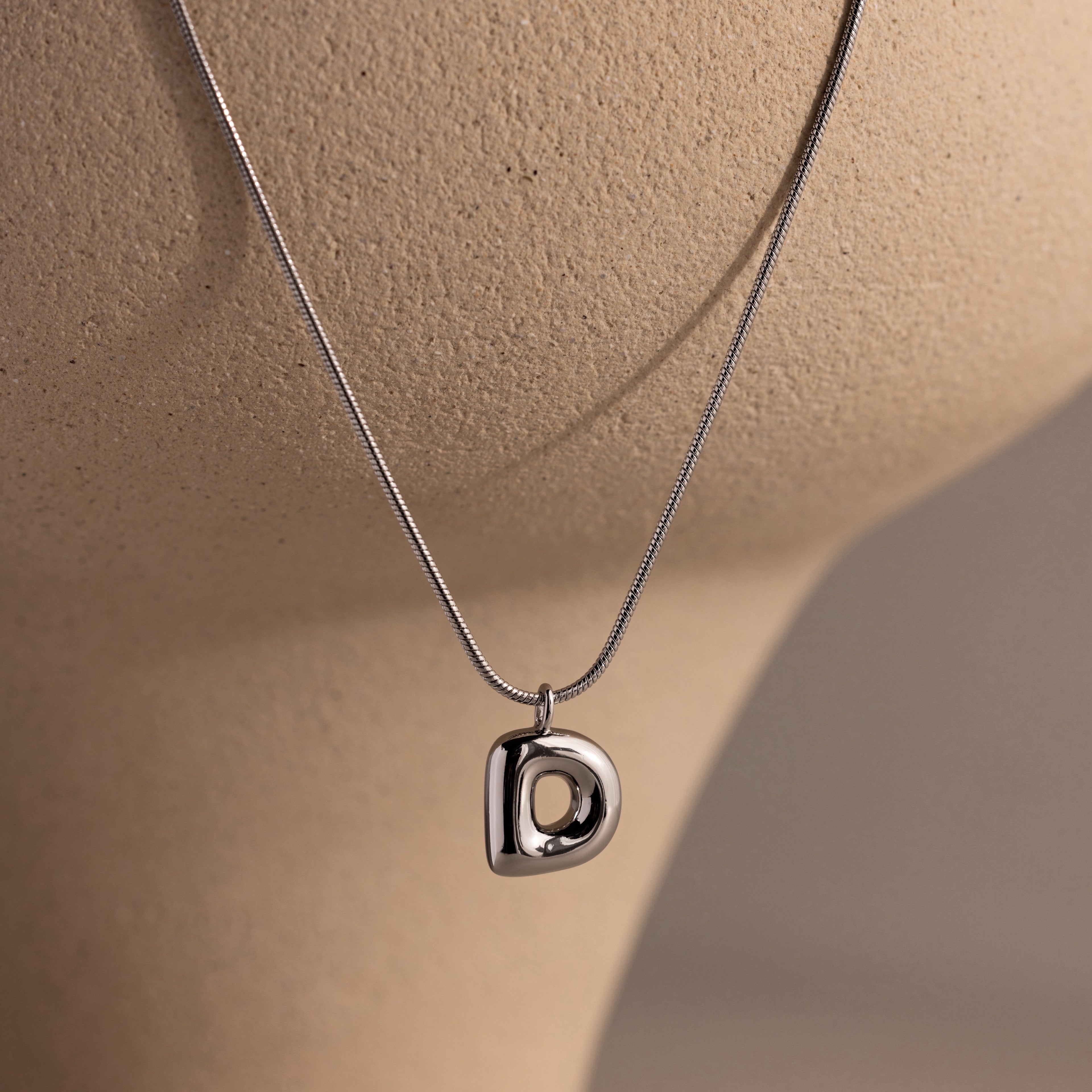 A Bubble Letter Necklace in White Gold with a polished D pendant is elegantly displayed on a beige bust.