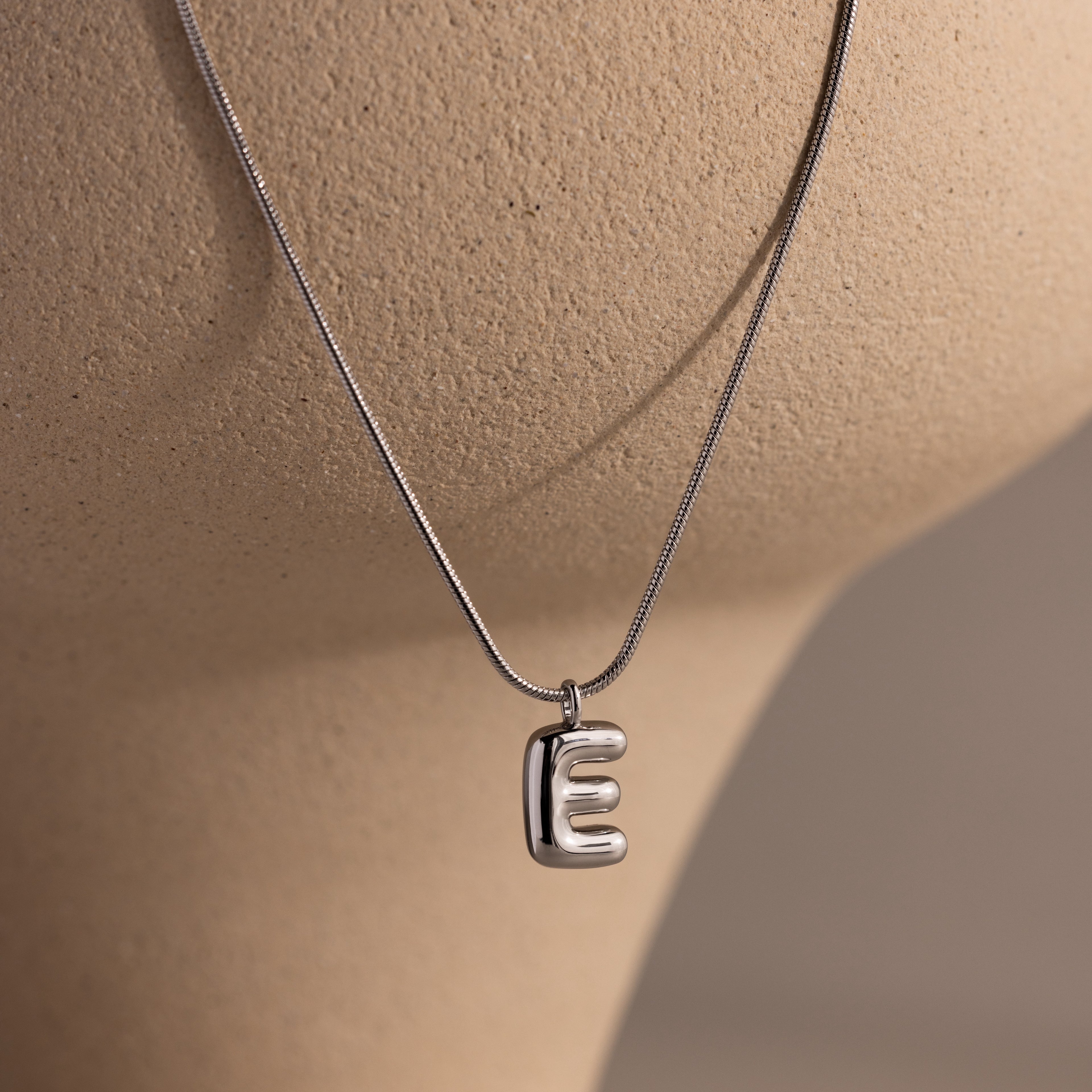 Bubble Letter Necklace in White Gold with a shiny E pendant, displayed on a beige mannequin bust—ideal for fans of personalized jewelry.