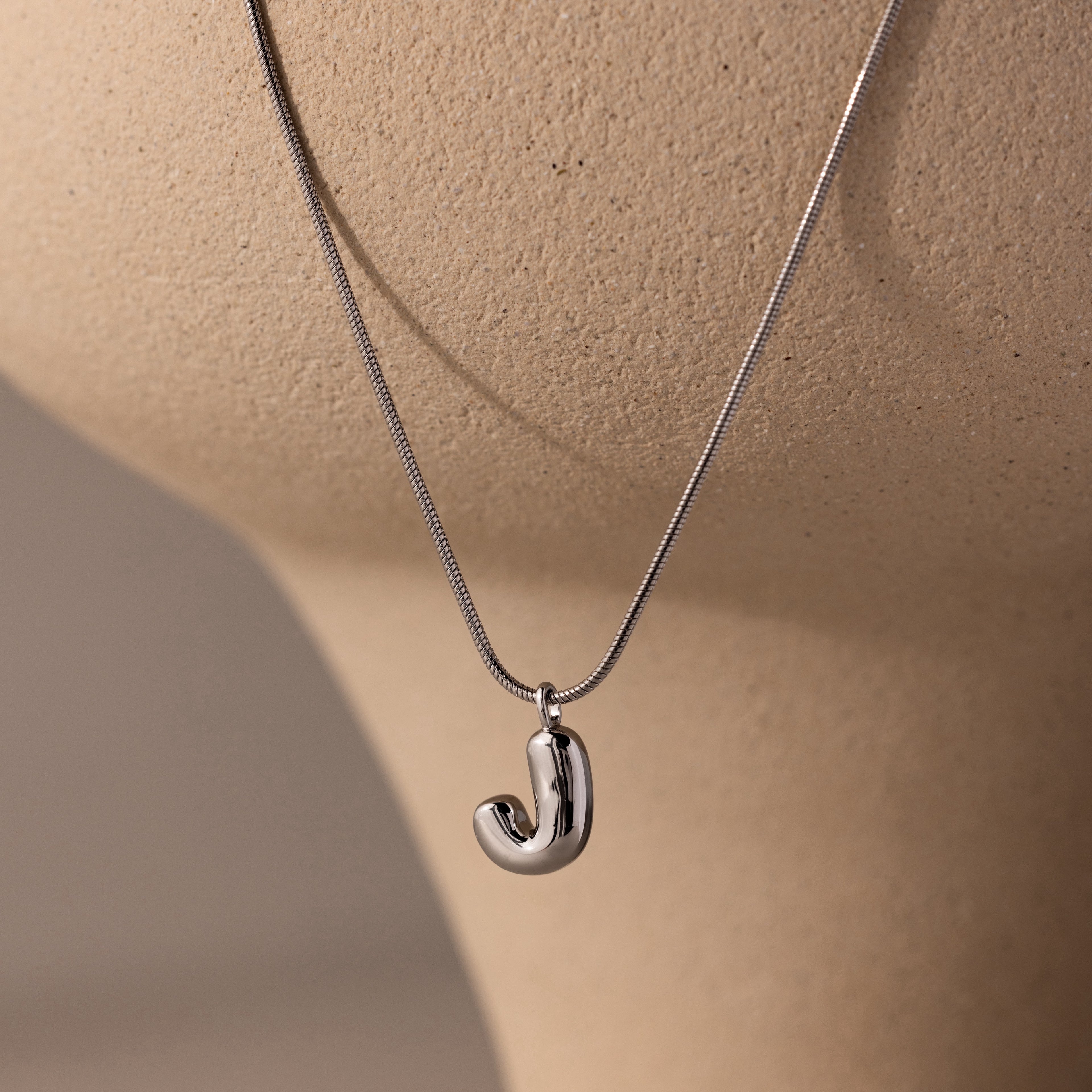 Bubble Letter Necklace in White Gold with a “J” pendant, shown on a beige mannequin bust—a chic personalized jewelry piece ideal for daily wear.