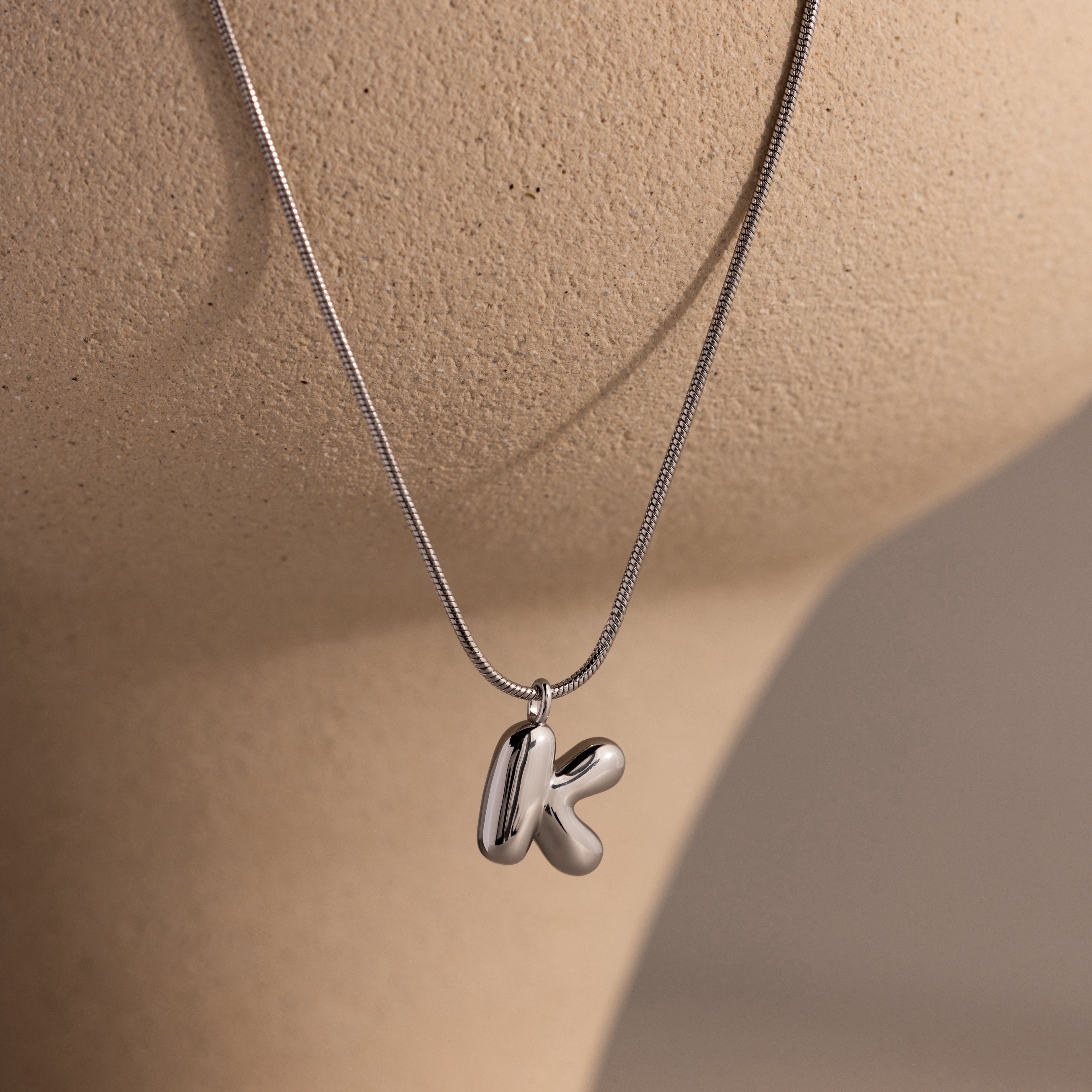 Bubble Letter Necklace in White Gold featuring two chunky metallic K charms, displayed on a beige mannequin bust—perfect for adding personalized flair to any look.