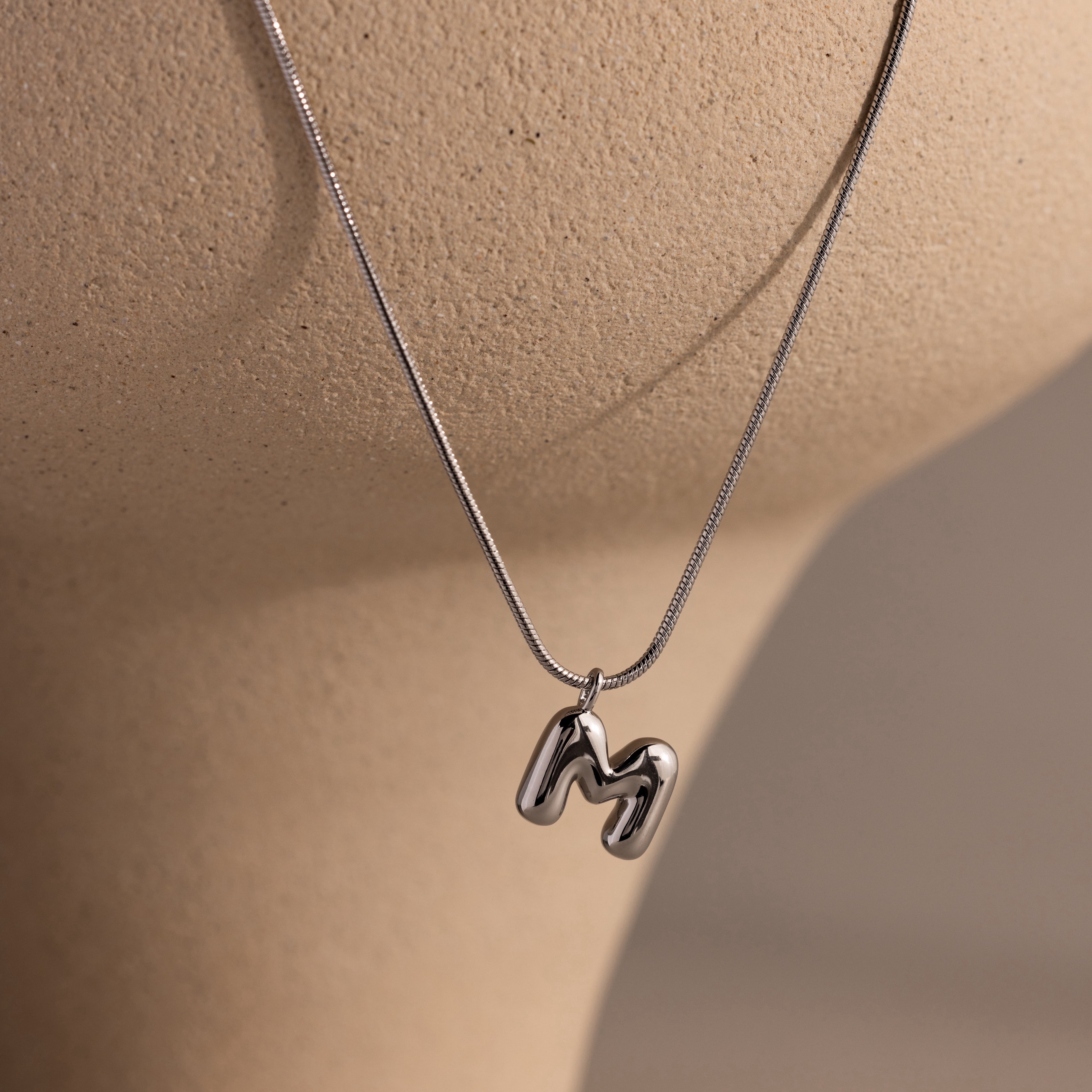 Personalized jewelry at its finest—a shiny Bubble Letter Necklace in White Gold with an M pendant elegantly displayed on a beige mannequin bust.