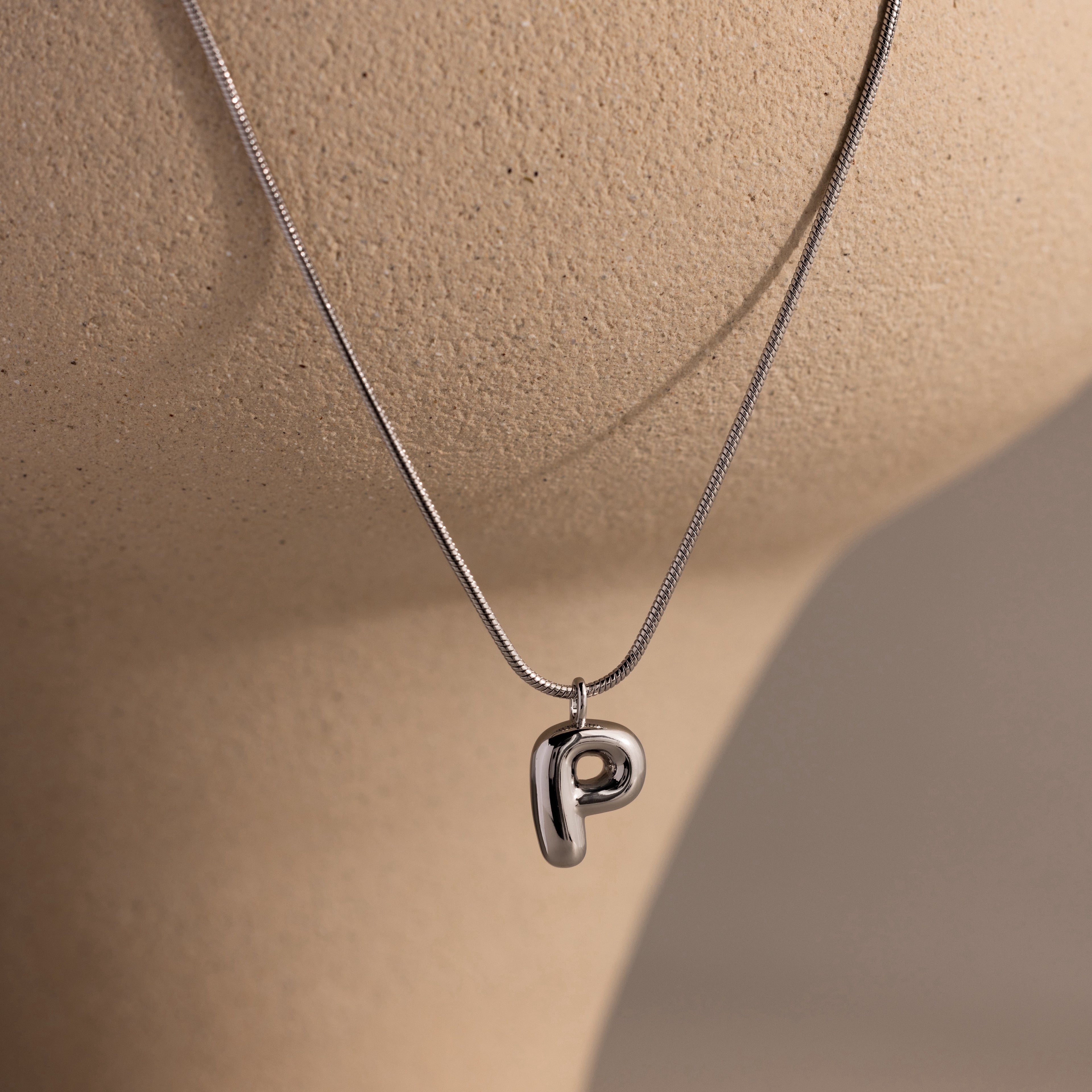 Bubble Letter Necklace in White Gold featuring a shiny letter P pendant, displayed on a beige textured mannequin bust—a perfect personalized jewelry piece.