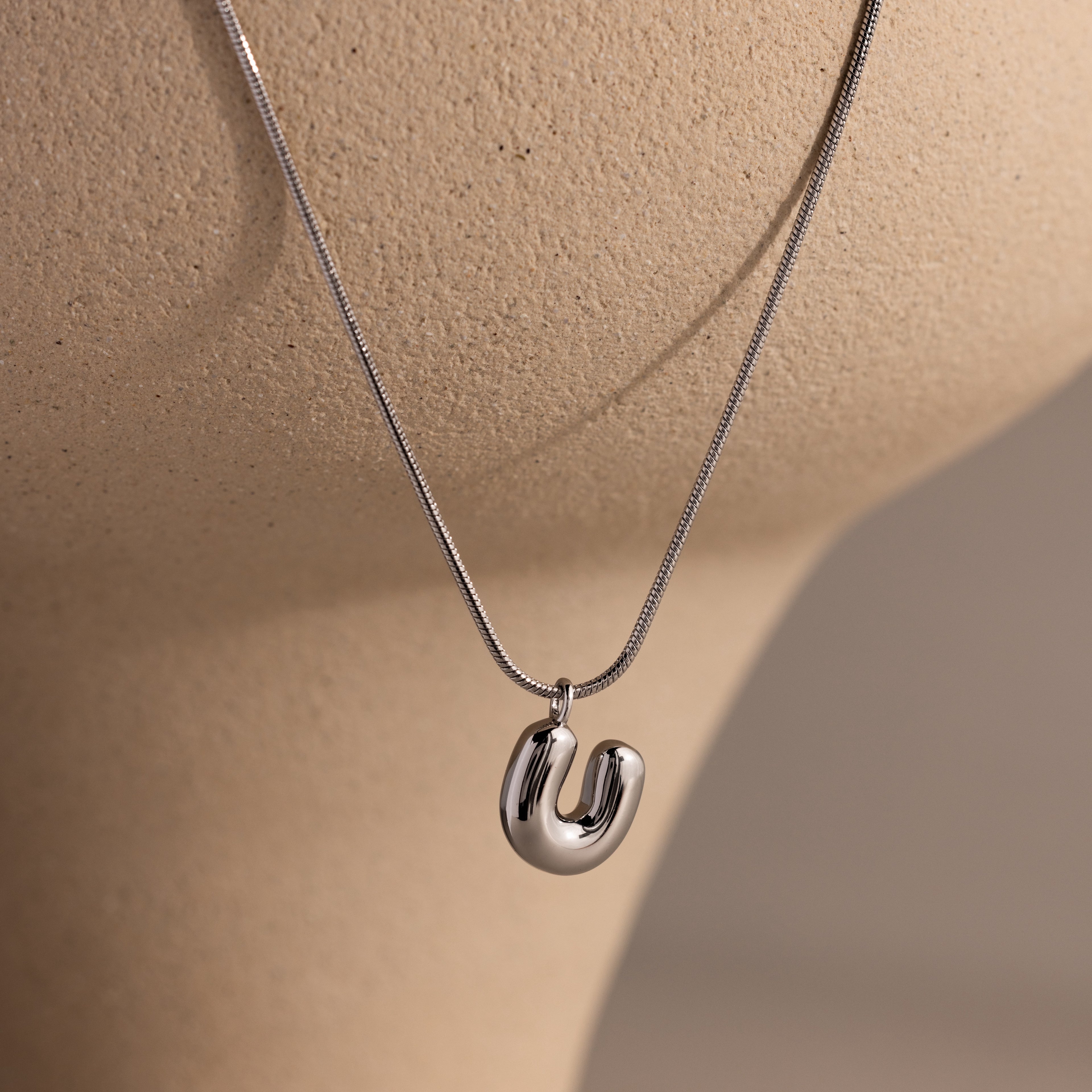 The Bubble Letter Necklace in White Gold features a modern, curved pendant displayed on a neutral mannequin bust—ideal for anyone who loves personalized jewelry with a stylish twist.