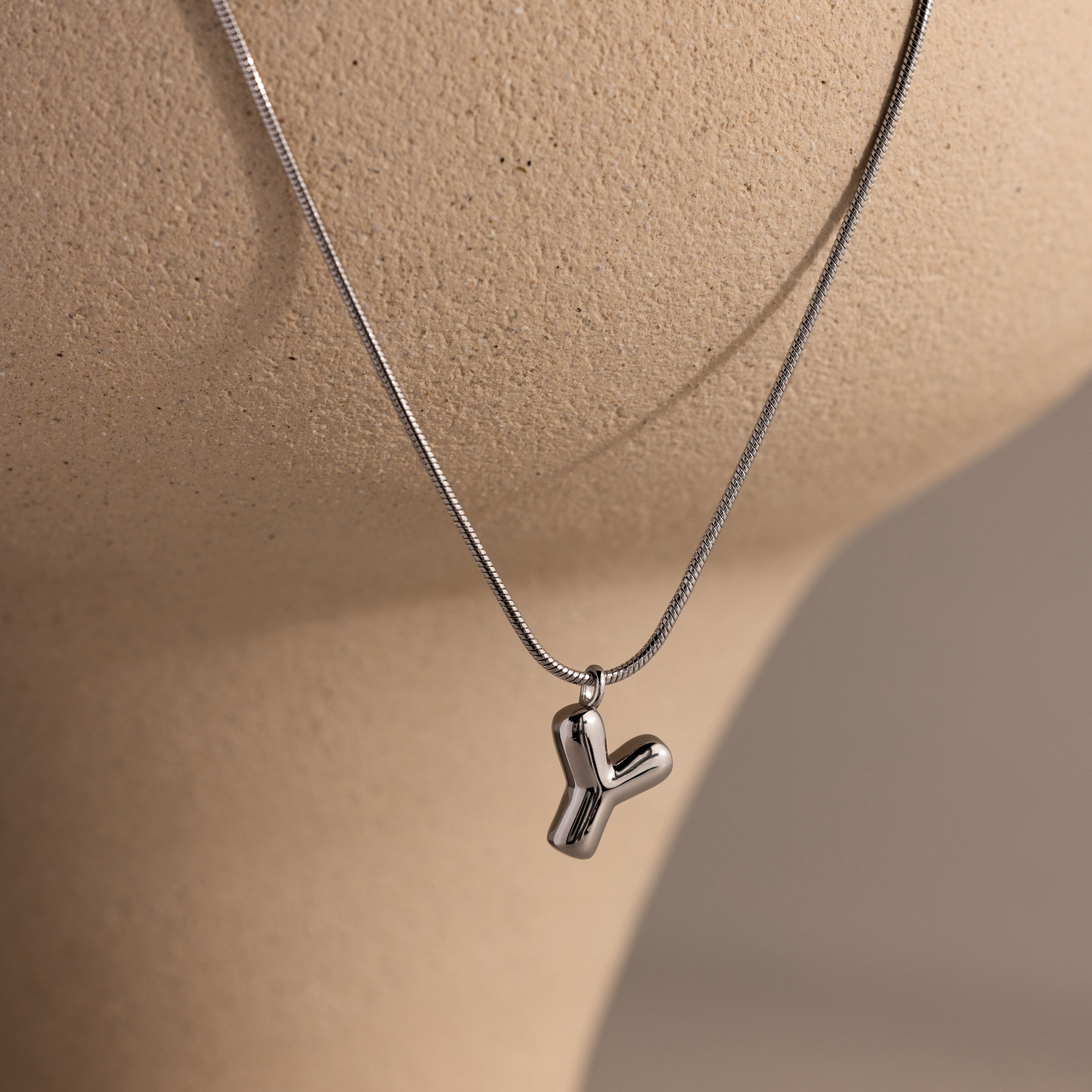 The Bubble Letter Necklace in White Gold features a Y-shaped pendant and is displayed on a beige mannequin bust.
