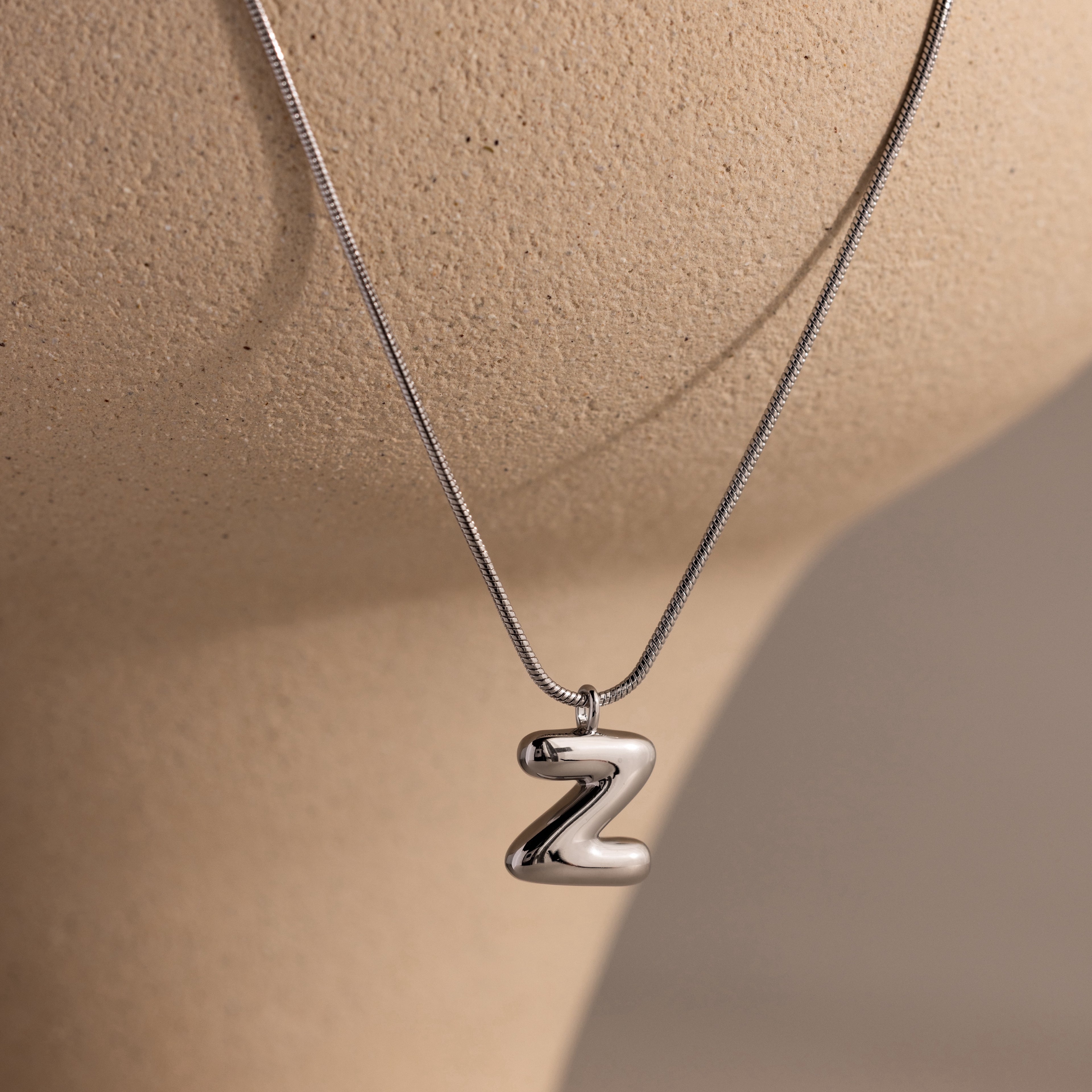 The Bubble Letter Necklace in White Gold, with a shiny Z pendant, is shown on a beige mannequin—an ideal choice for lovers of personalized jewelry.