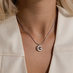 A woman wears a Bubble Letter Necklace in White Gold with a G pendant, paired with a cream-colored blazer for a chic, personalized jewelry look.