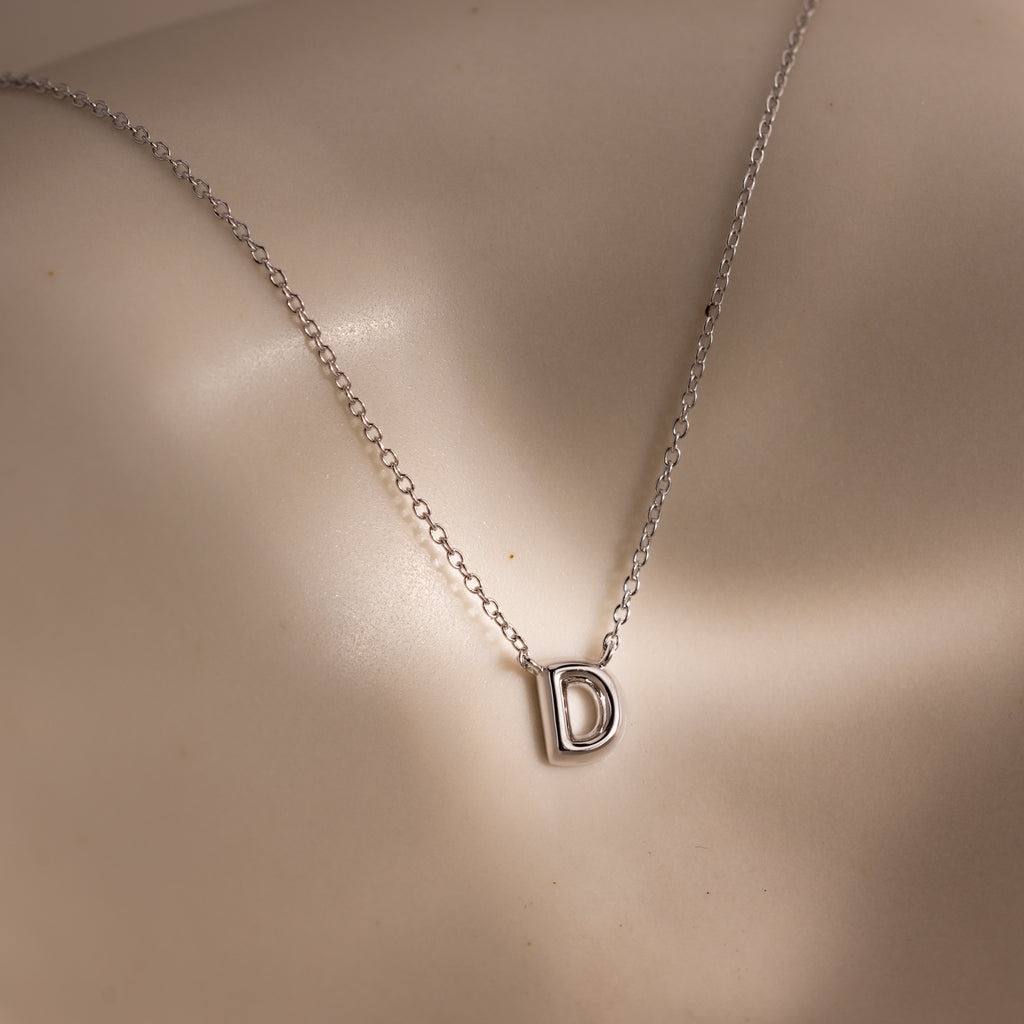 The Dainty Bubble Letter Necklace in Sterling Silver features a minimalist chain with a letter D pendant, elegantly displayed against smooth, light-colored skin.