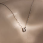 The Dainty Bubble Letter Necklace in Sterling Silver features a minimalist chain with a letter D pendant, elegantly displayed against smooth, light-colored skin.