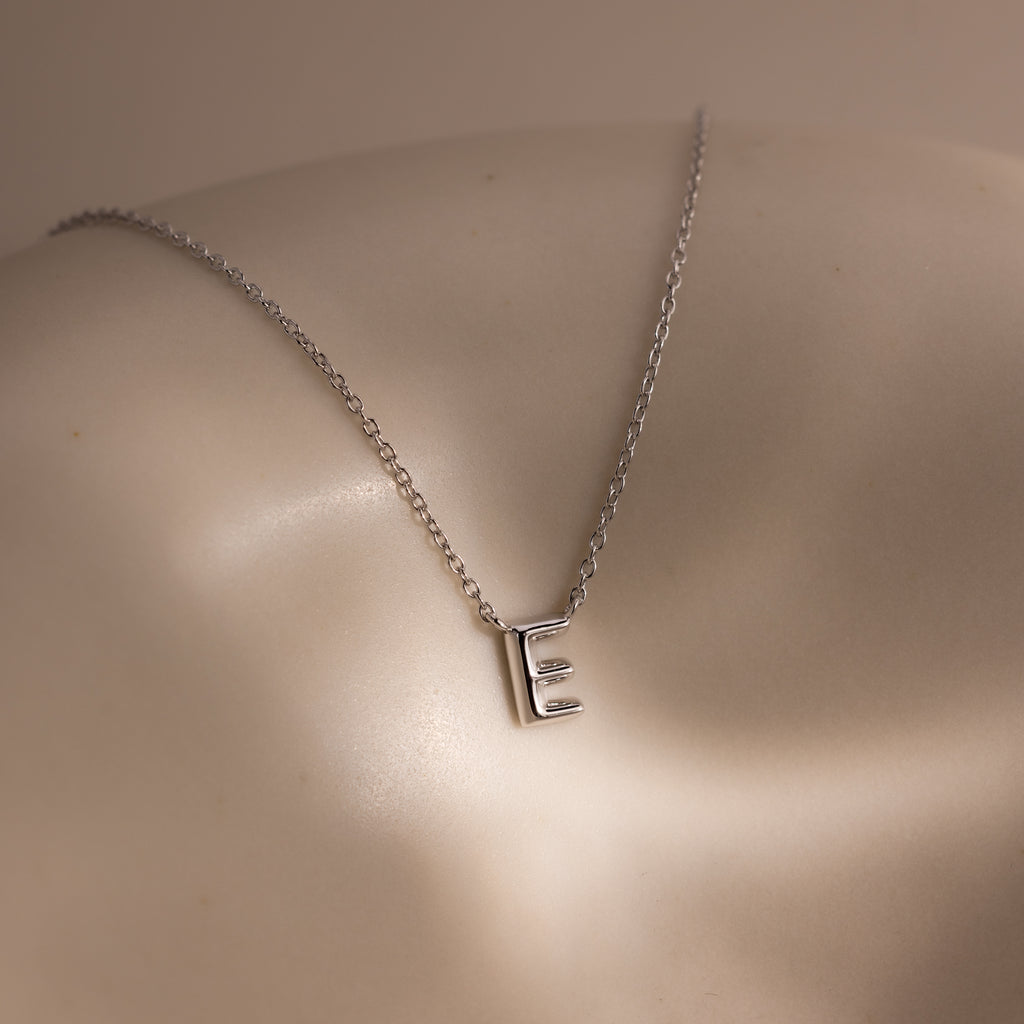 The Dainty Bubble Letter Necklace in Sterling Silver, shown with an "E" pendant on a smooth neutral background, is the perfect personalized minimalist accessory.