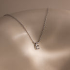 The Dainty Bubble Letter Necklace in Sterling Silver, shown with an "E" pendant on a smooth neutral background, is the perfect personalized minimalist accessory.